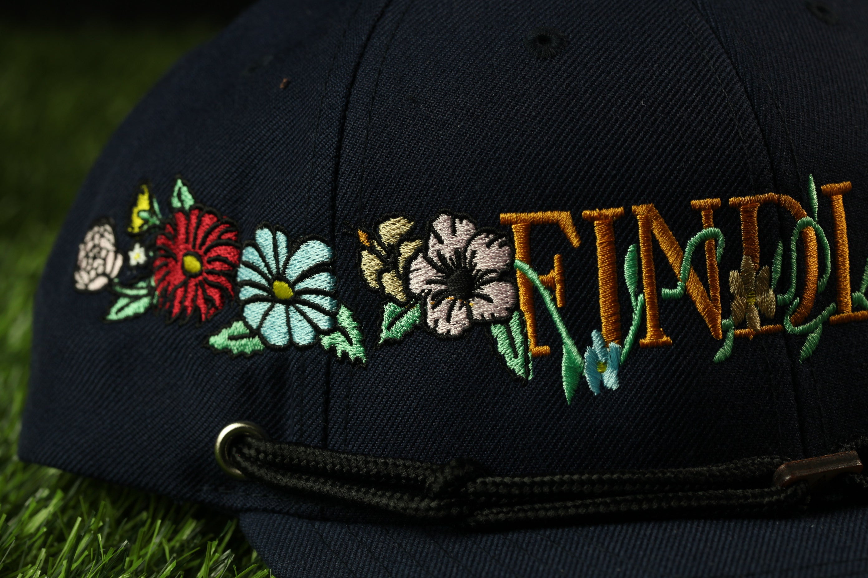 A close-up view of a black baseball cap with colorful floral embroidery on the brim.