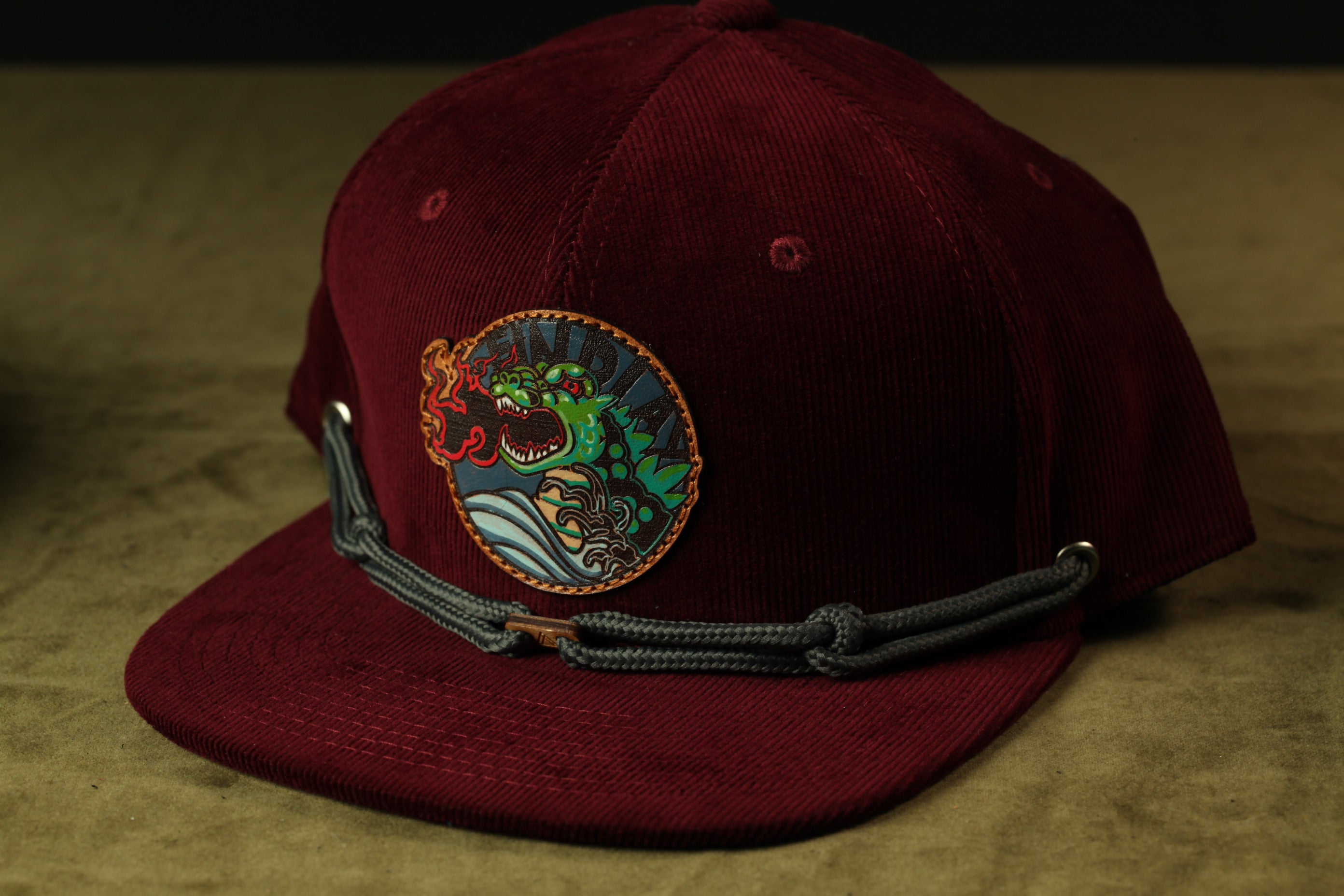 A burgundy baseball cap with a colorful dragon design on the front.