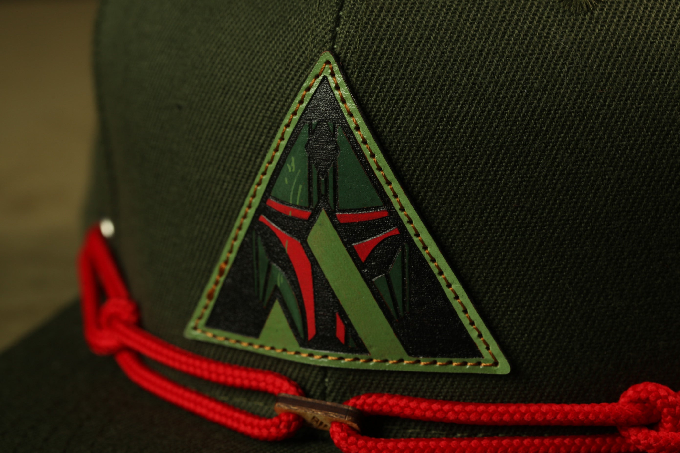 A close-up view of a dark green fabric with a red and black triangular patch featuring a stylized design on it.