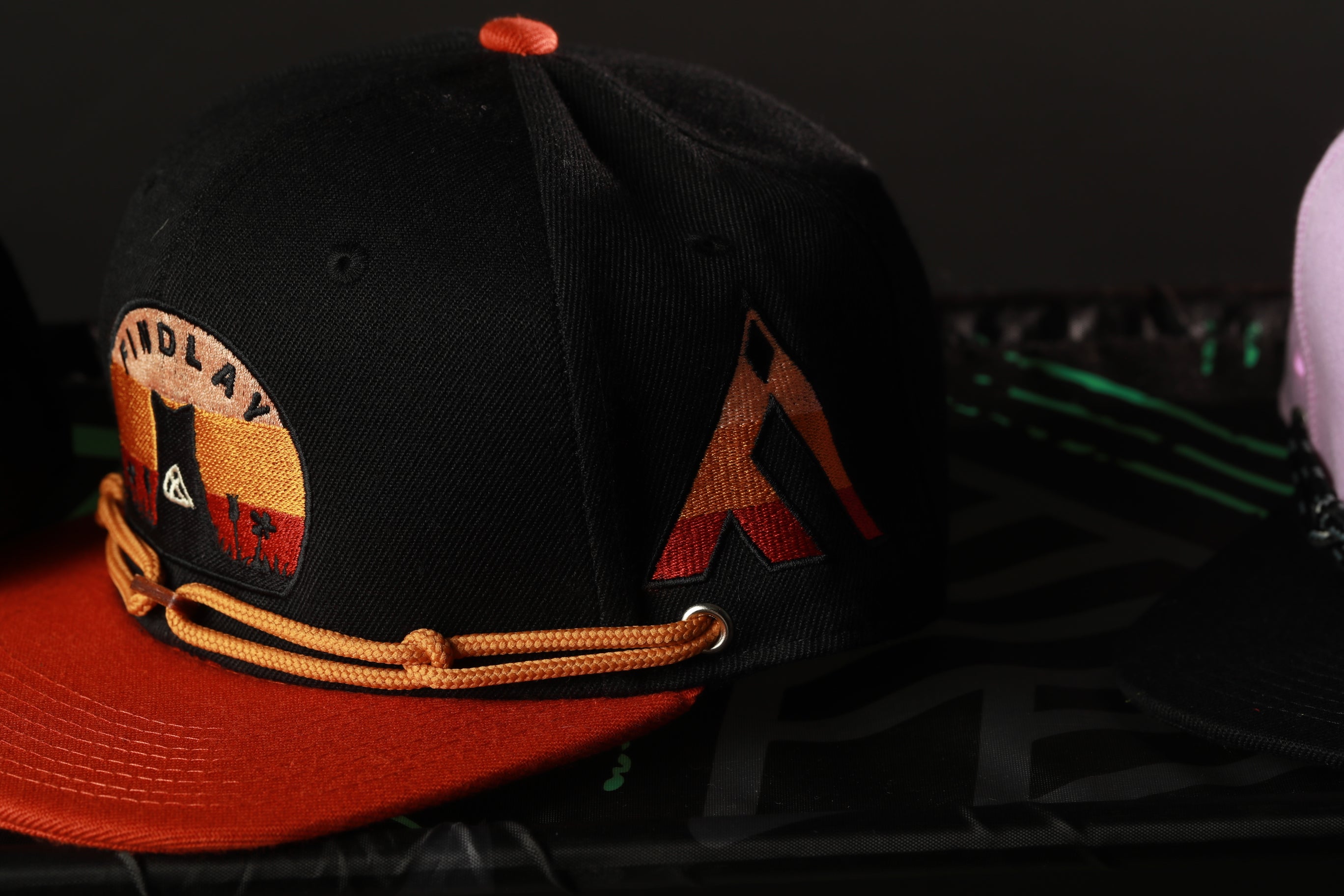 A close-up view of a black baseball cap with a red brim and a logo on the front, resting on a black surface.
