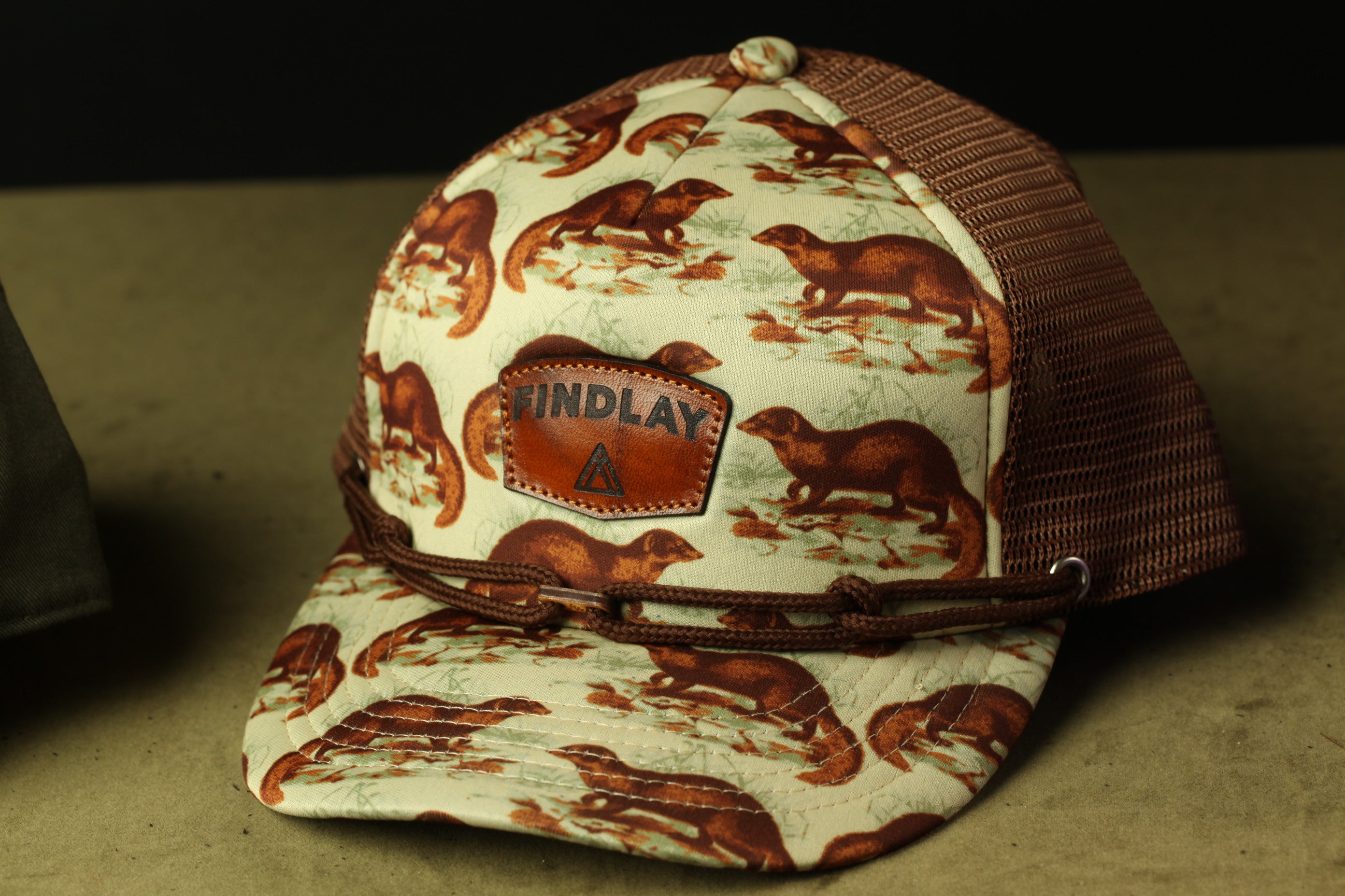 A baseball cap with a pattern of brown otters printed on it, featuring a leather patch with the word "FINDLAY" printed on it.