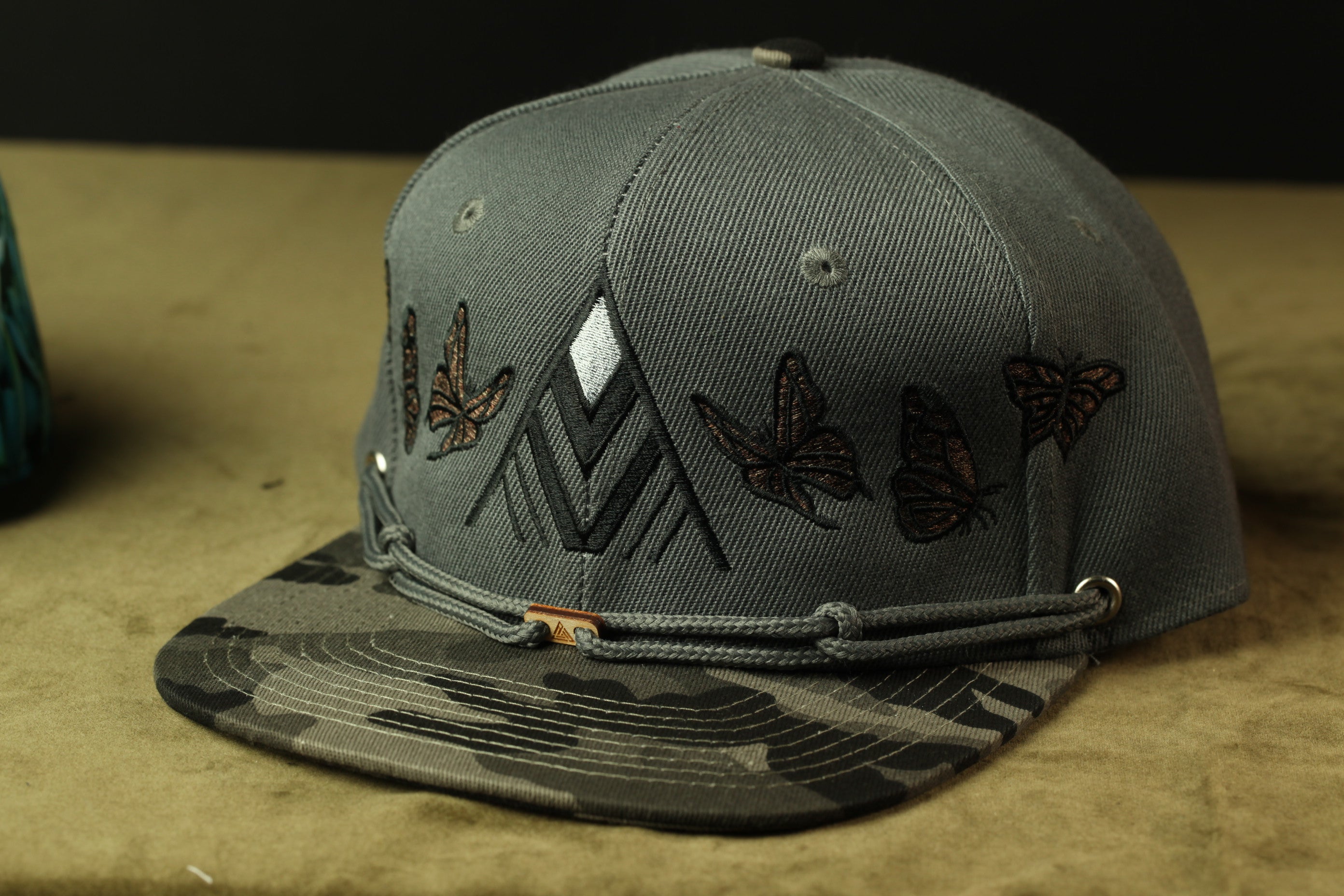 A gray baseball cap with a camouflage pattern and butterfly designs on the front.