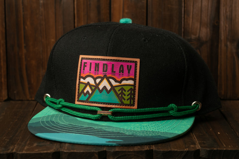 A black baseball cap with a colorful graphic patch on the front, featuring a mountain landscape design.
