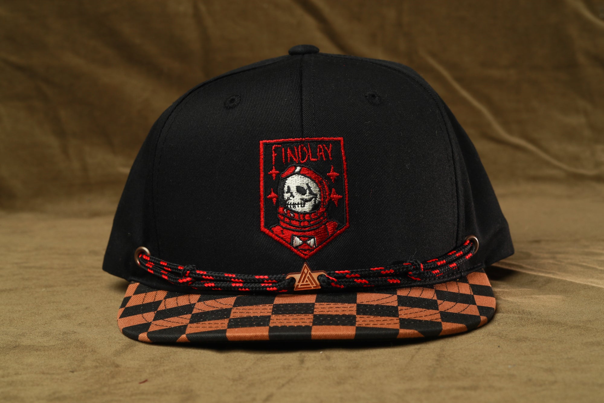 A black baseball cap with a red and white checkered pattern and a skull embroidered on the front.