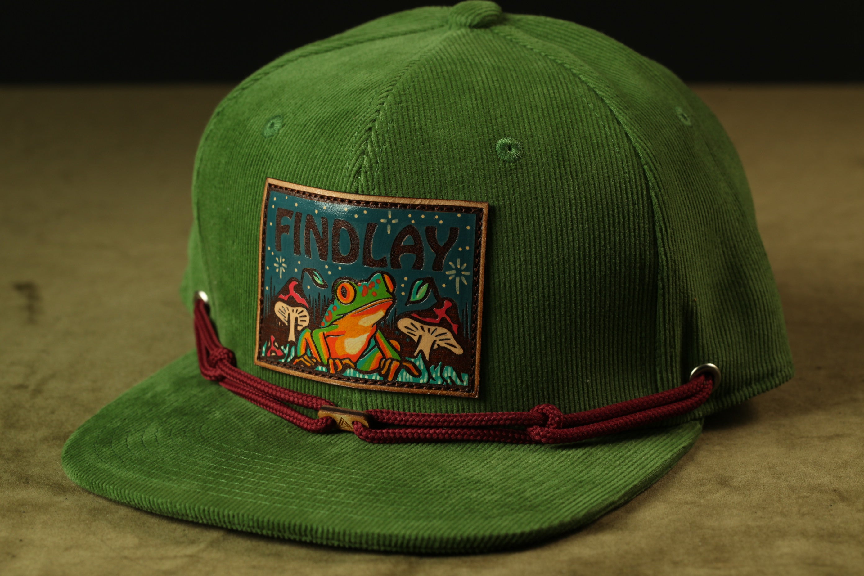 A green baseball cap with a patch featuring a frog and mushrooms.