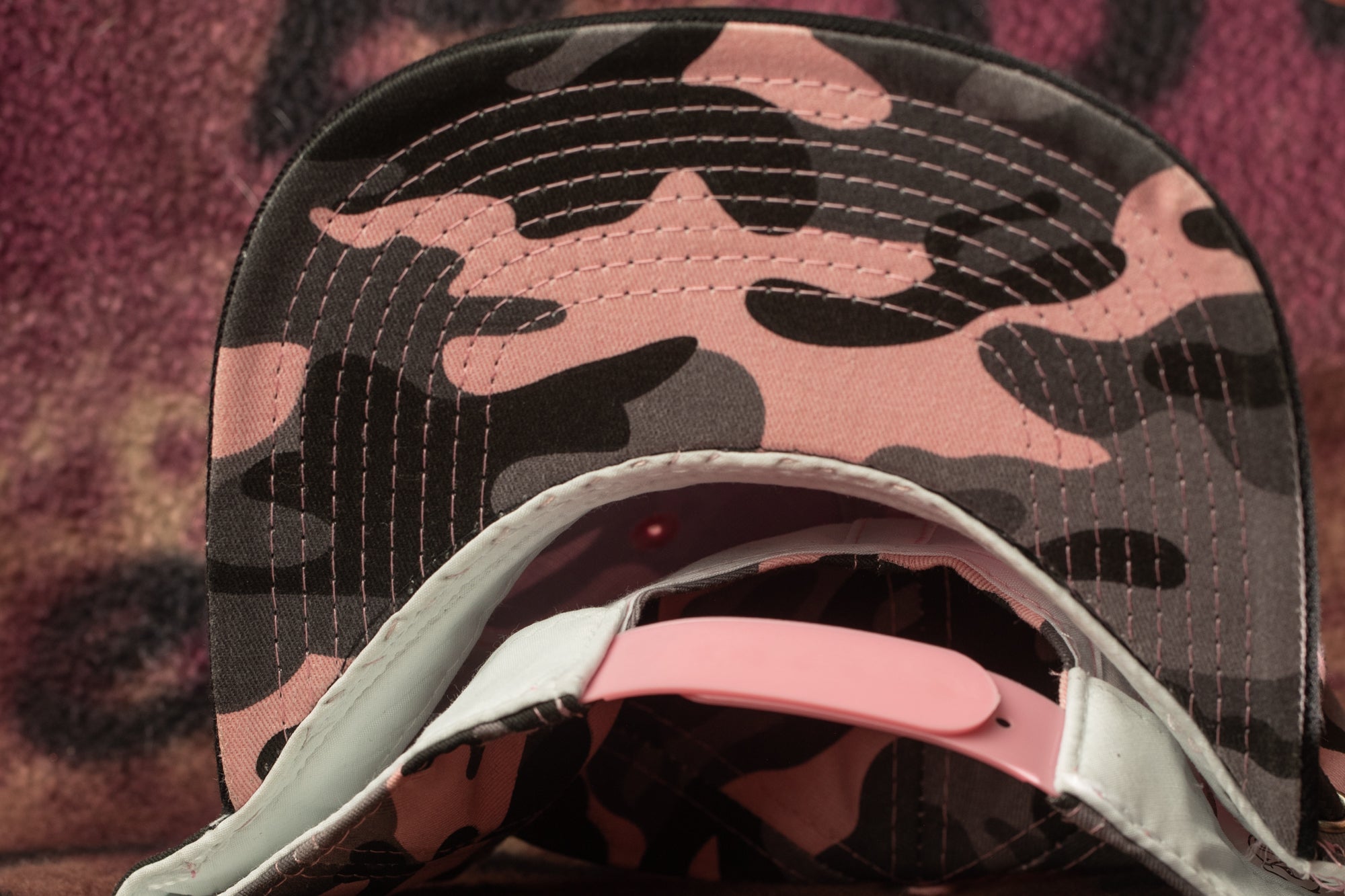 A close-up view of a camouflage baseball cap with a pink strap.