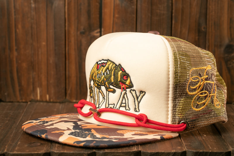 A white baseball cap with a camouflage pattern and a red string, featuring an embroidered image of a fish on the front.