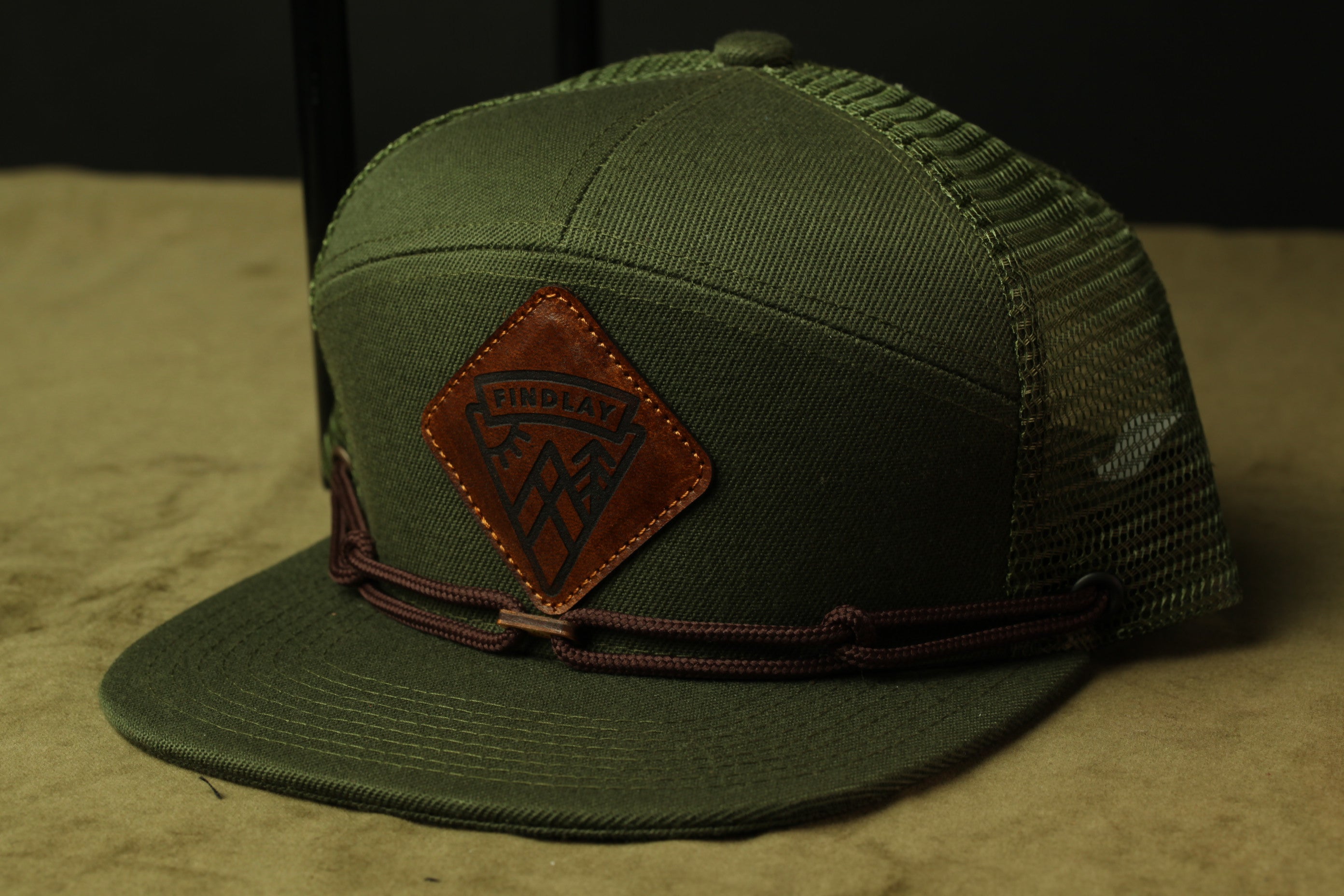 A green baseball cap with a brown leather patch on the front, featuring a logo.