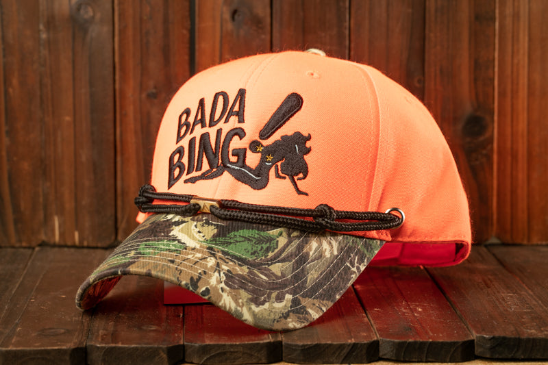 An orange baseball cap with the text "Bada Bing" printed on it, placed on a wooden surface.