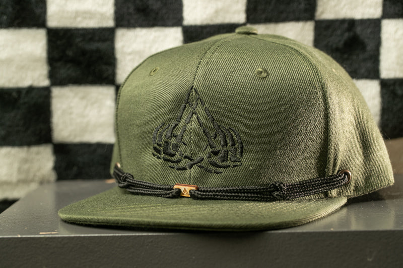 A green baseball cap with a black embroidered logo on the front, sitting on a surface against a black and white checkered background.