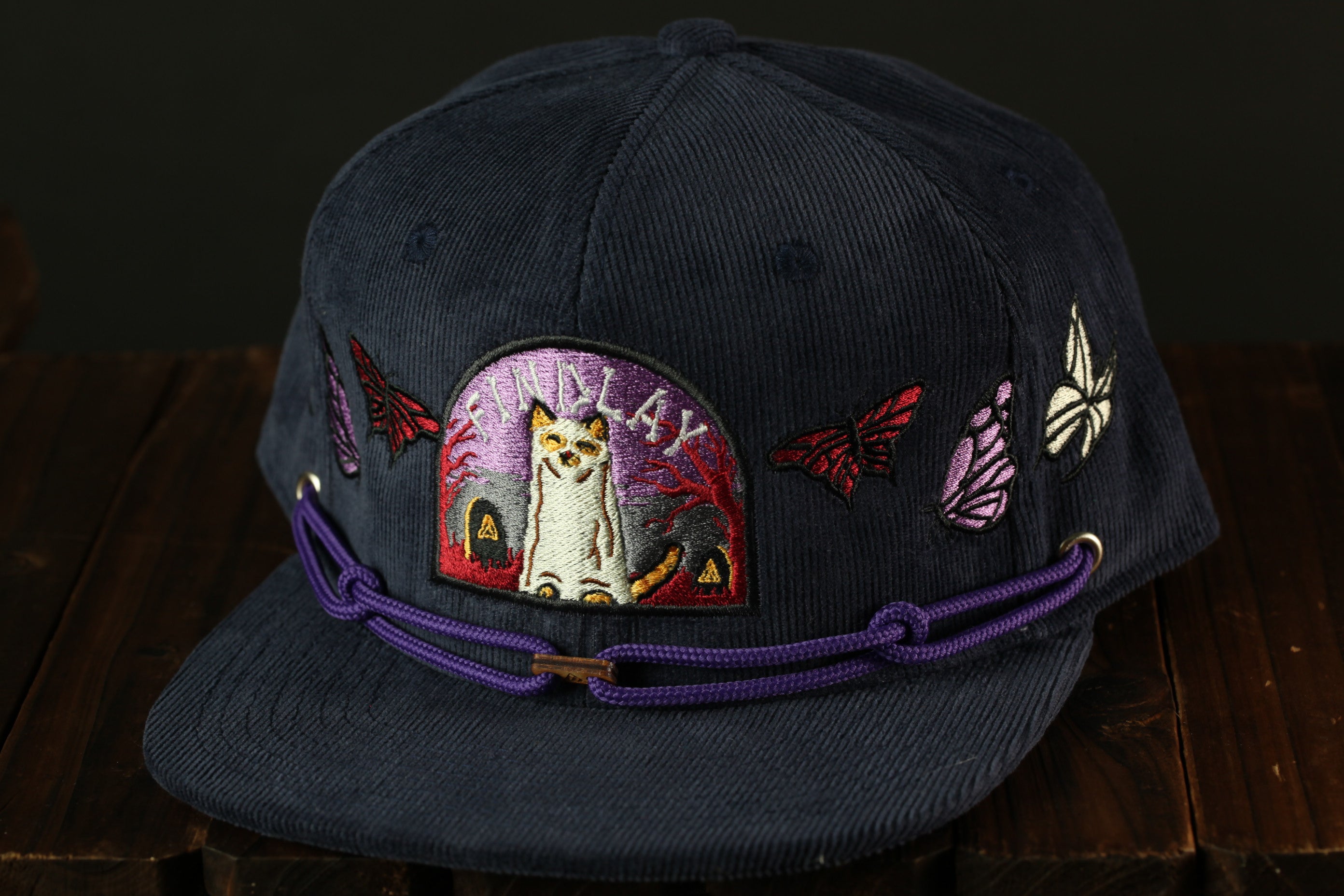 A dark blue baseball cap with a purple string and various colorful patches, including a cat and butterflies, on the front.