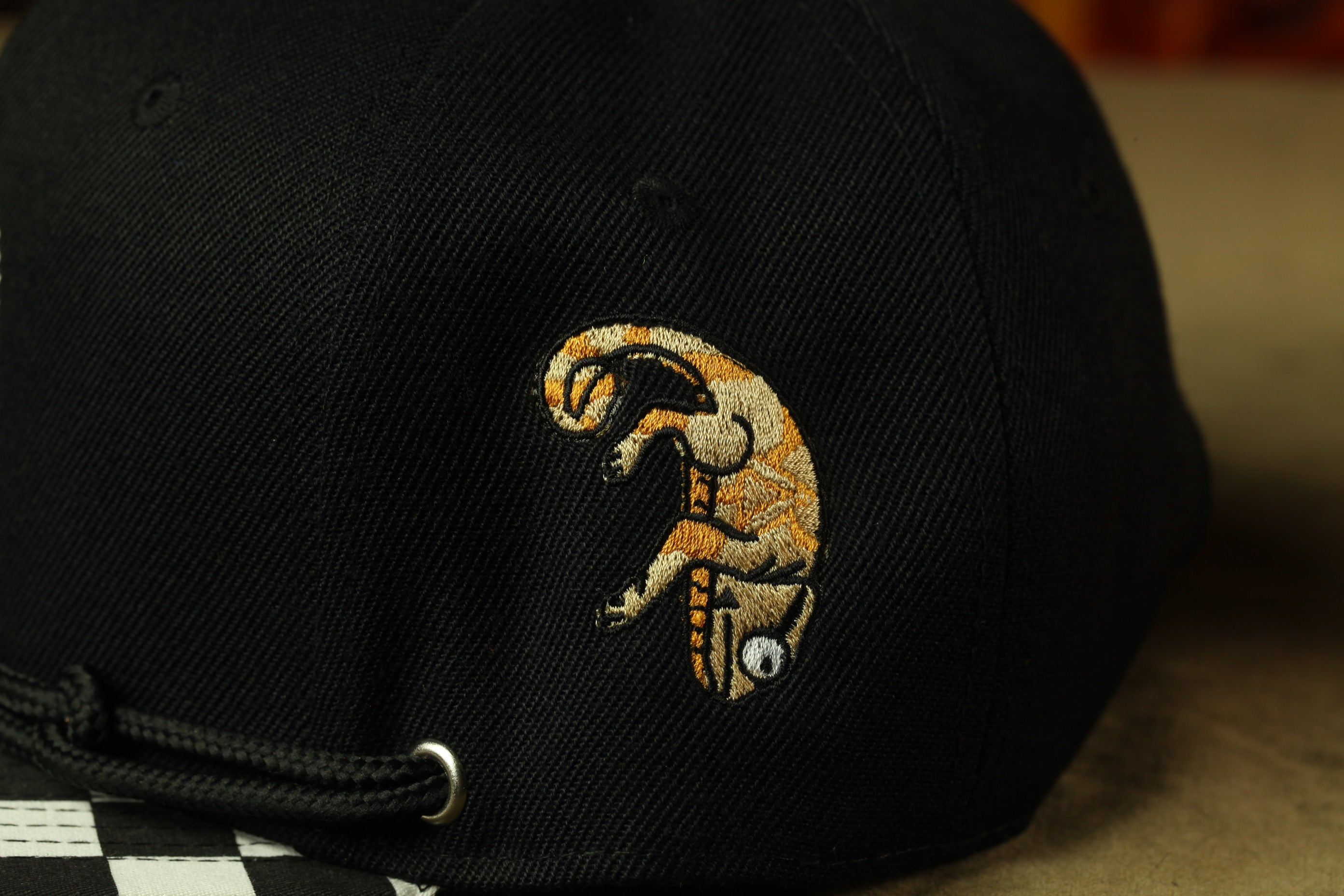 A close-up view of a black baseball cap with an embroidered design of a chameleon on the front.
