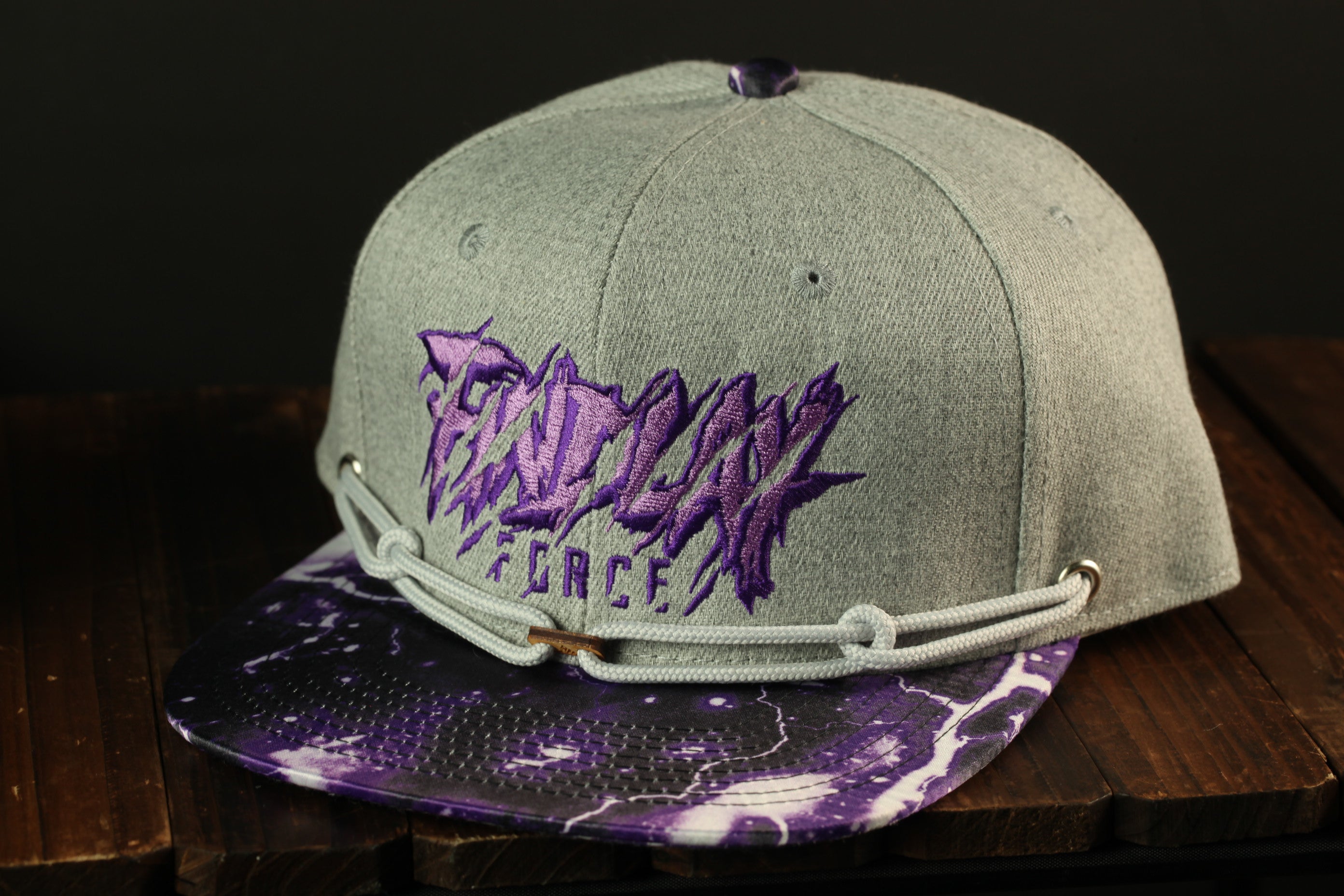 A gray baseball cap with purple text and graphics, sitting on a wooden surface.