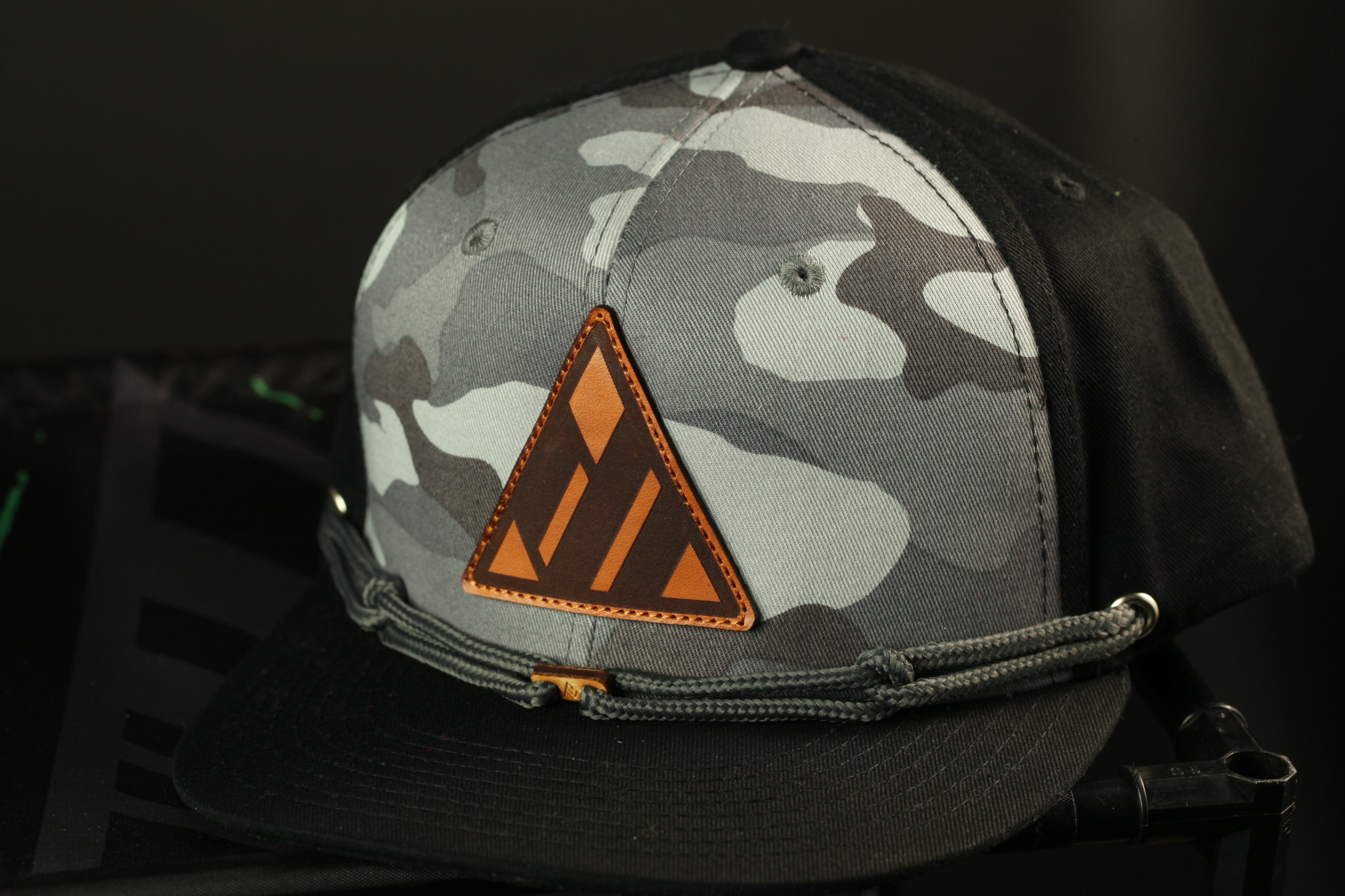 A black and gray camouflage baseball cap with a triangular patch on the front.