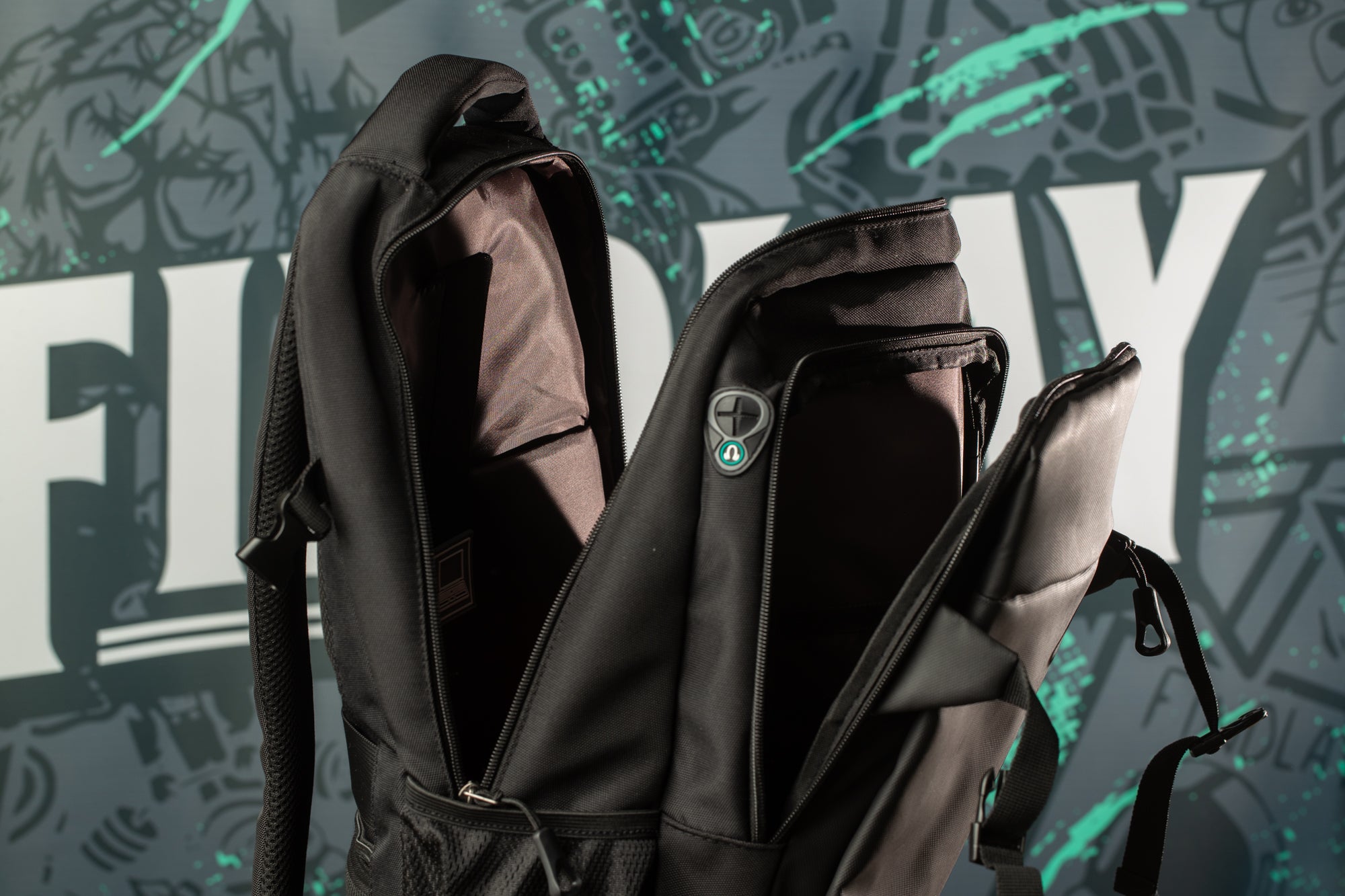 A black backpack with a zipper and a small green logo on the front, placed against a colorful graffiti-style background.