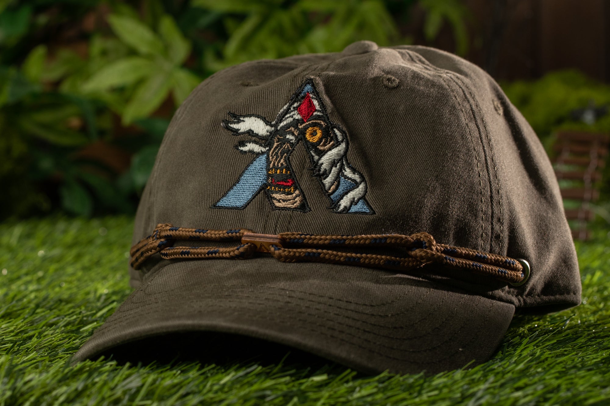 A brown baseball cap with a colorful embroidered letter "A" on it, resting on a grassy surface.