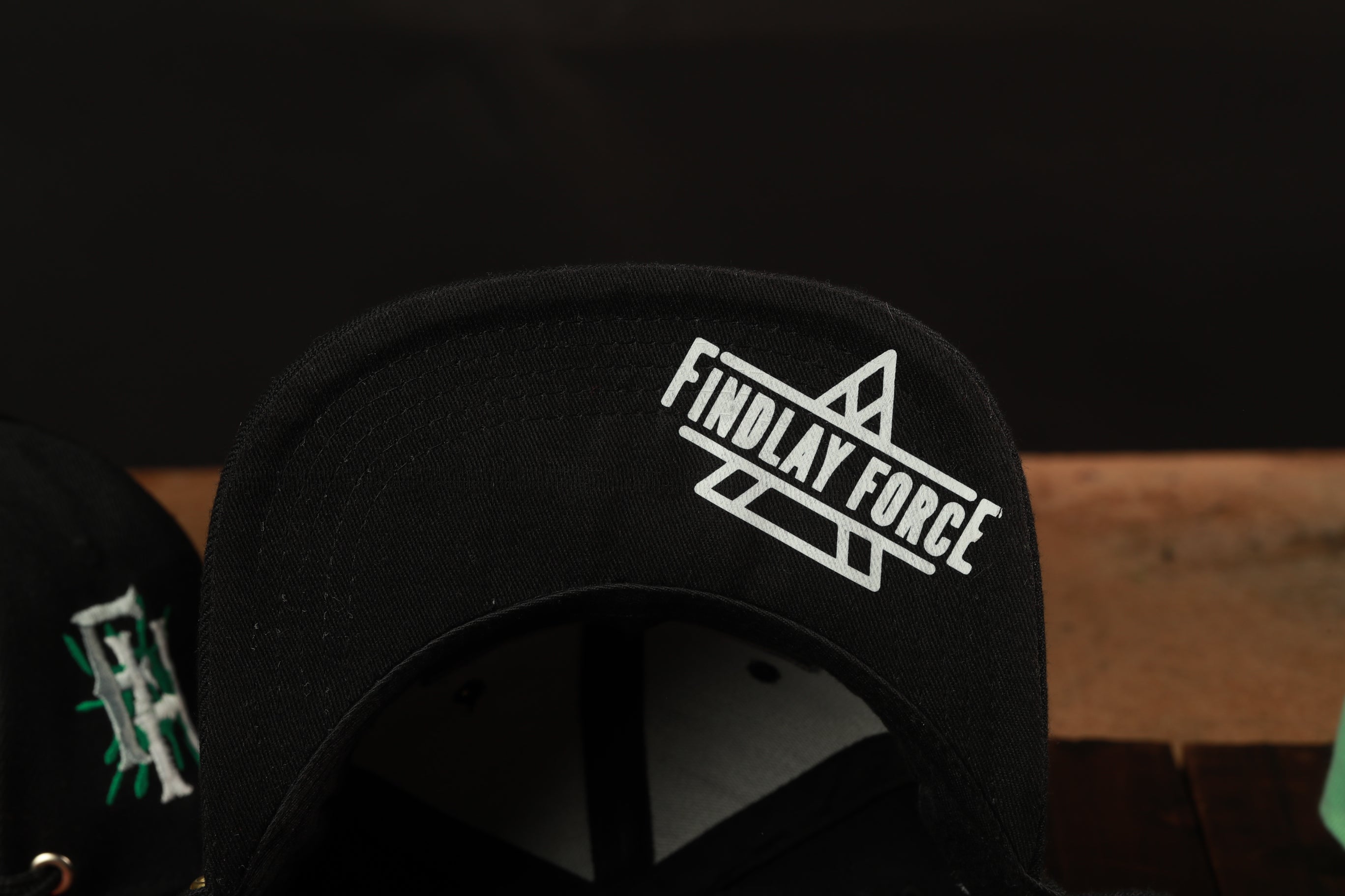 A close-up view of a black baseball cap with the text "FINDLAY FORCE" printed on it.