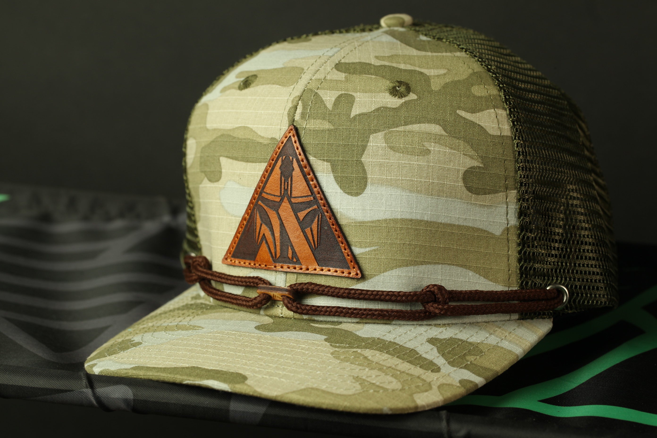 A camouflage baseball cap with a leather patch and a brown leather strap.