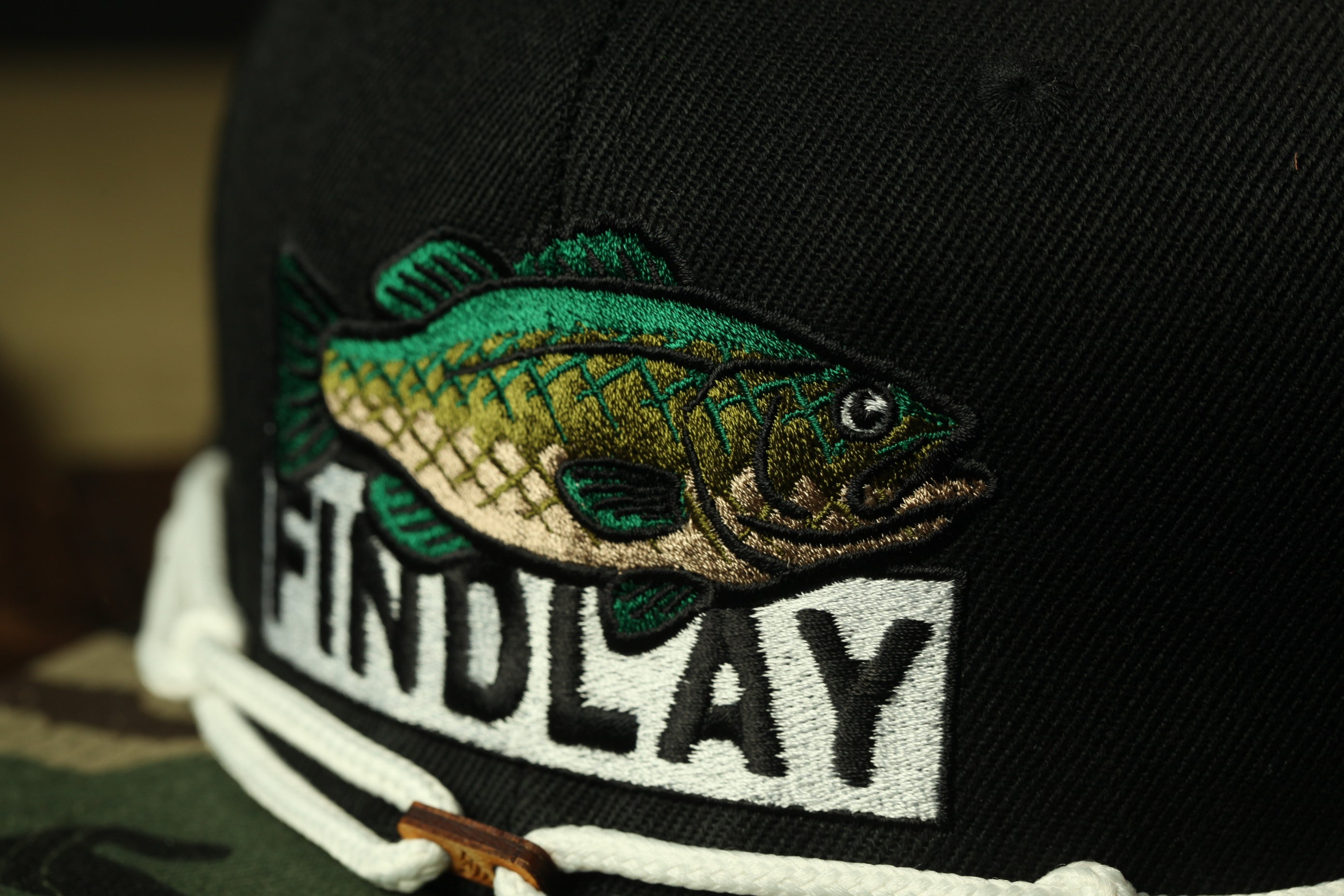 A close-up of a black baseball cap with a fish embroidered on it, and the word "FINDlay" printed on the front.