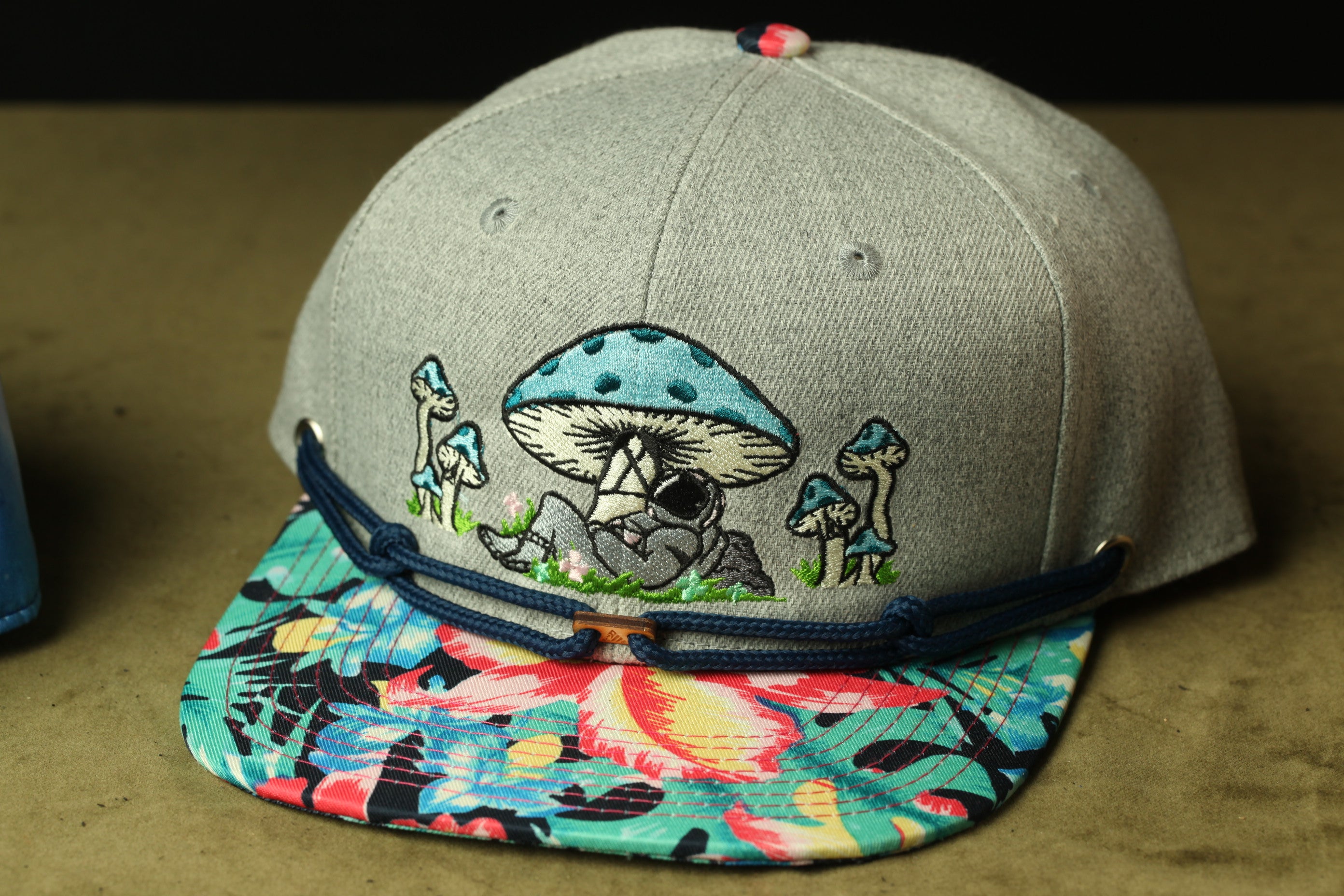 A gray baseball cap with a colorful floral pattern and a cartoon mushroom design on the front.