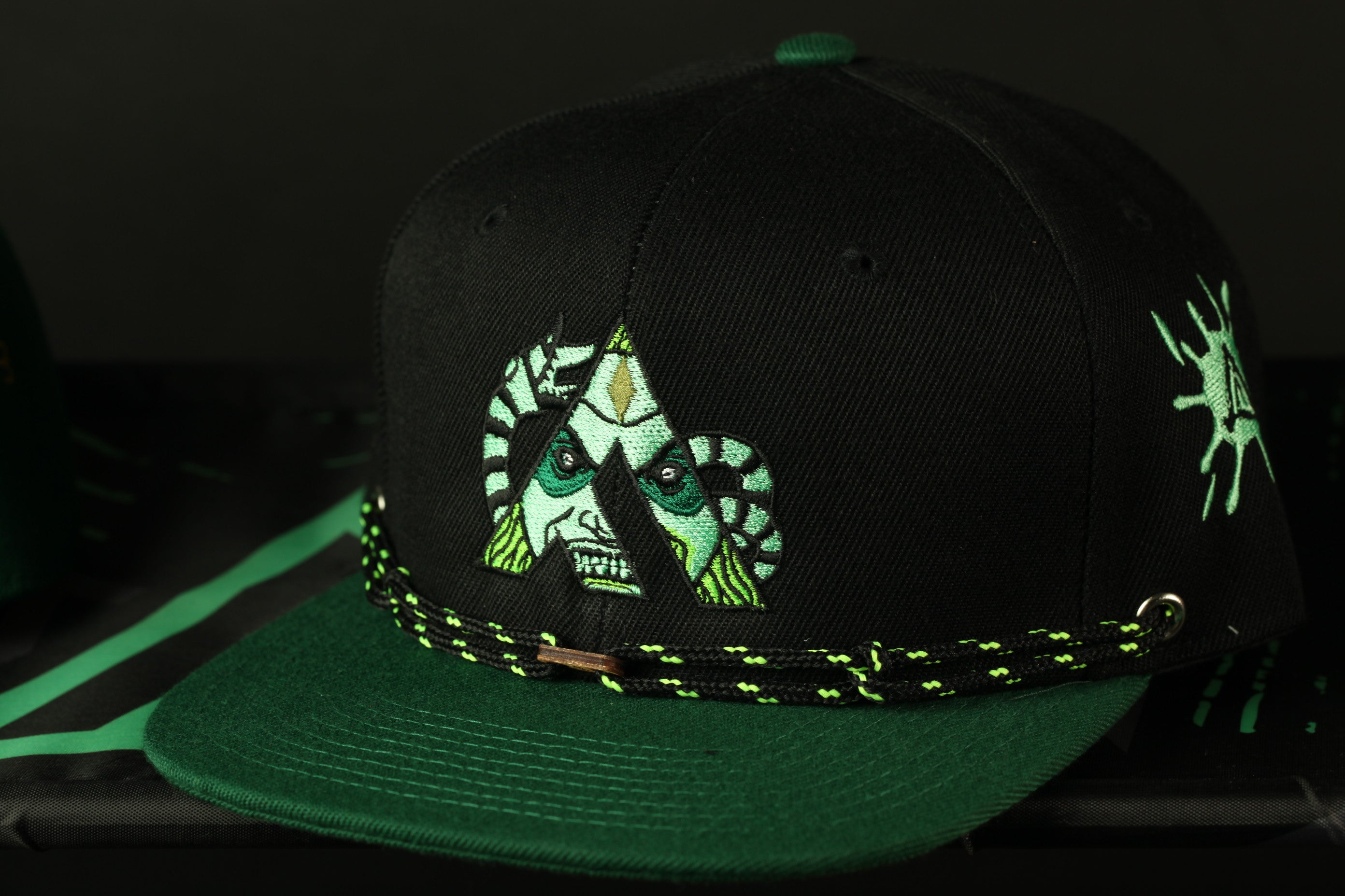 A black baseball cap with a green brim and a unique design featuring a face with a snake-like pattern.