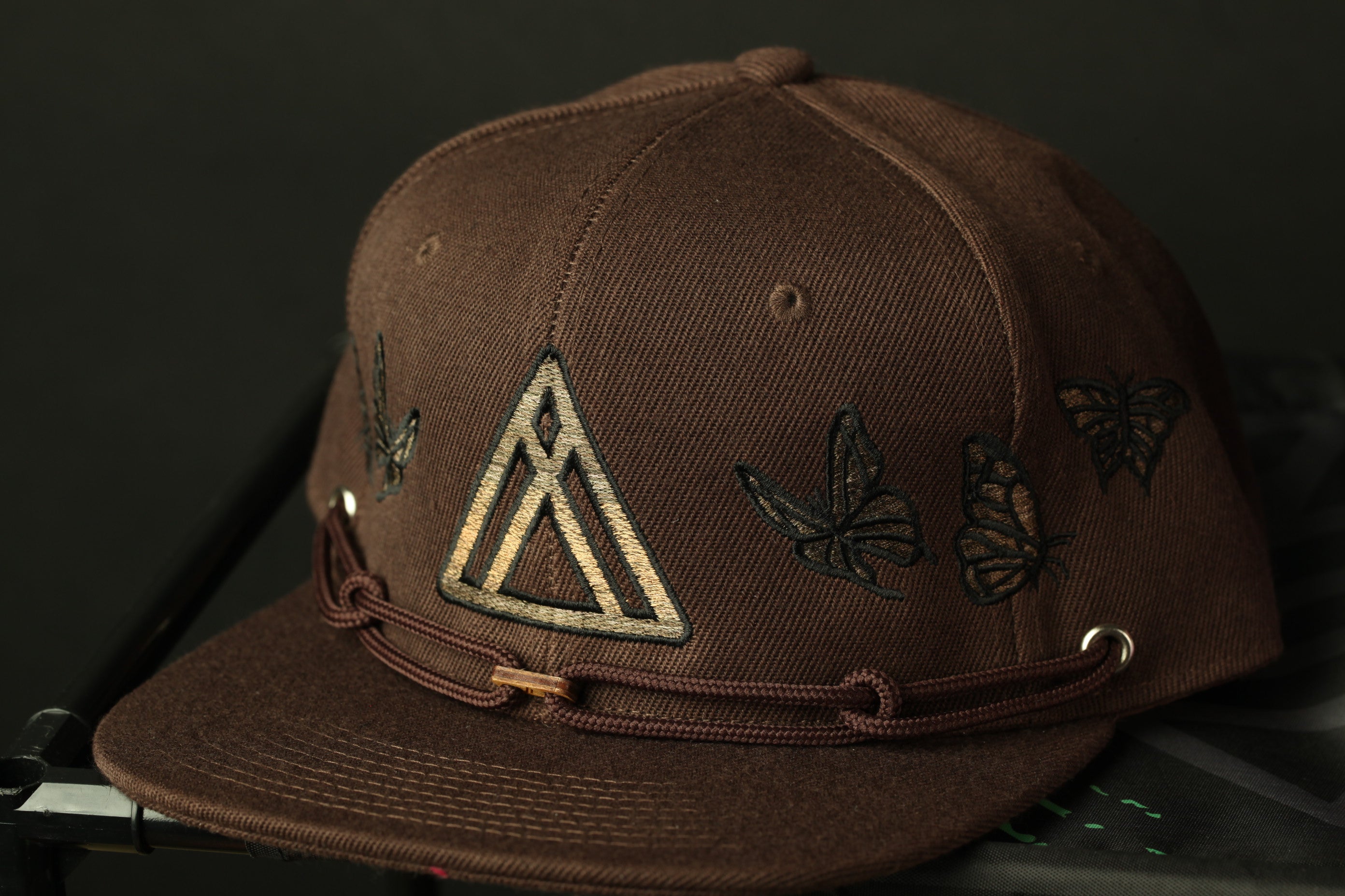 A brown baseball cap with a triangular logo and butterflies printed on it.
