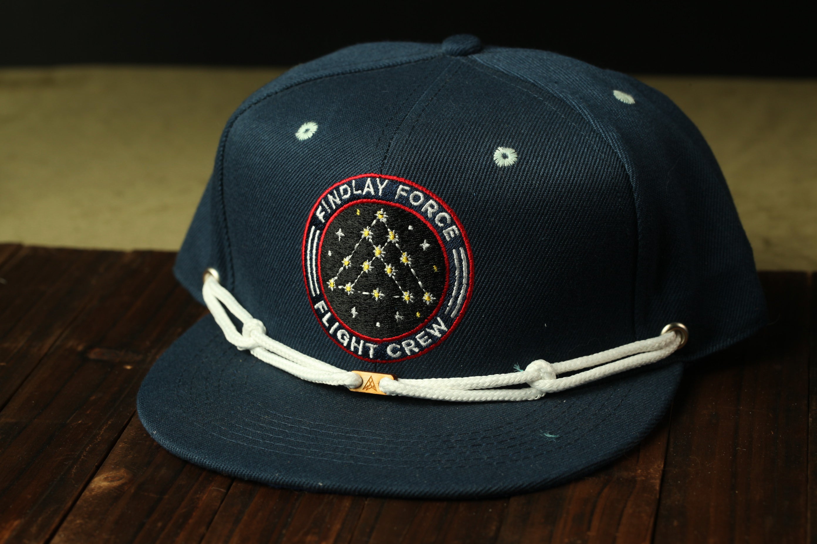 A navy blue baseball cap with a circular patch on the front, featuring a starry design and the text "FINDLAY FORCE FLIGHT CREW".