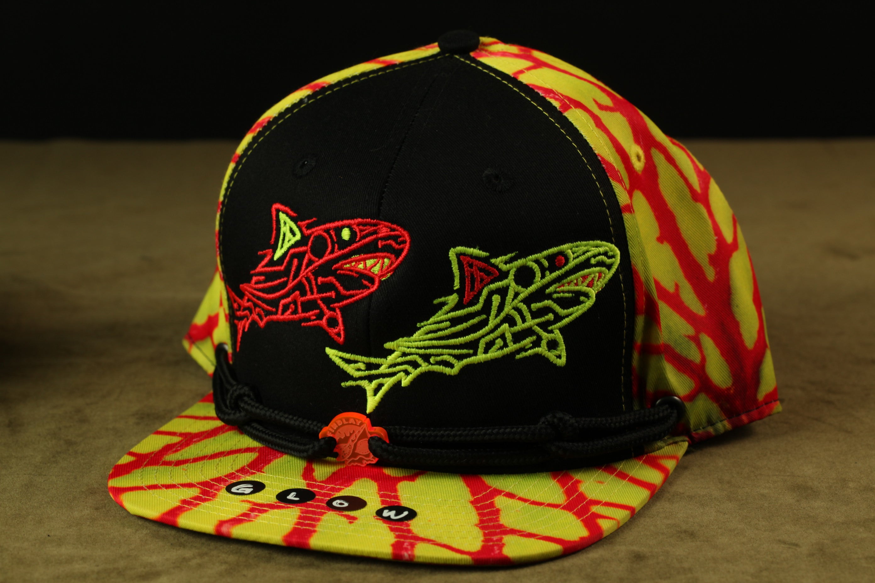 A colorful baseball cap with a black brim and a yellow brim, featuring a design of two sharks in red and green colors.