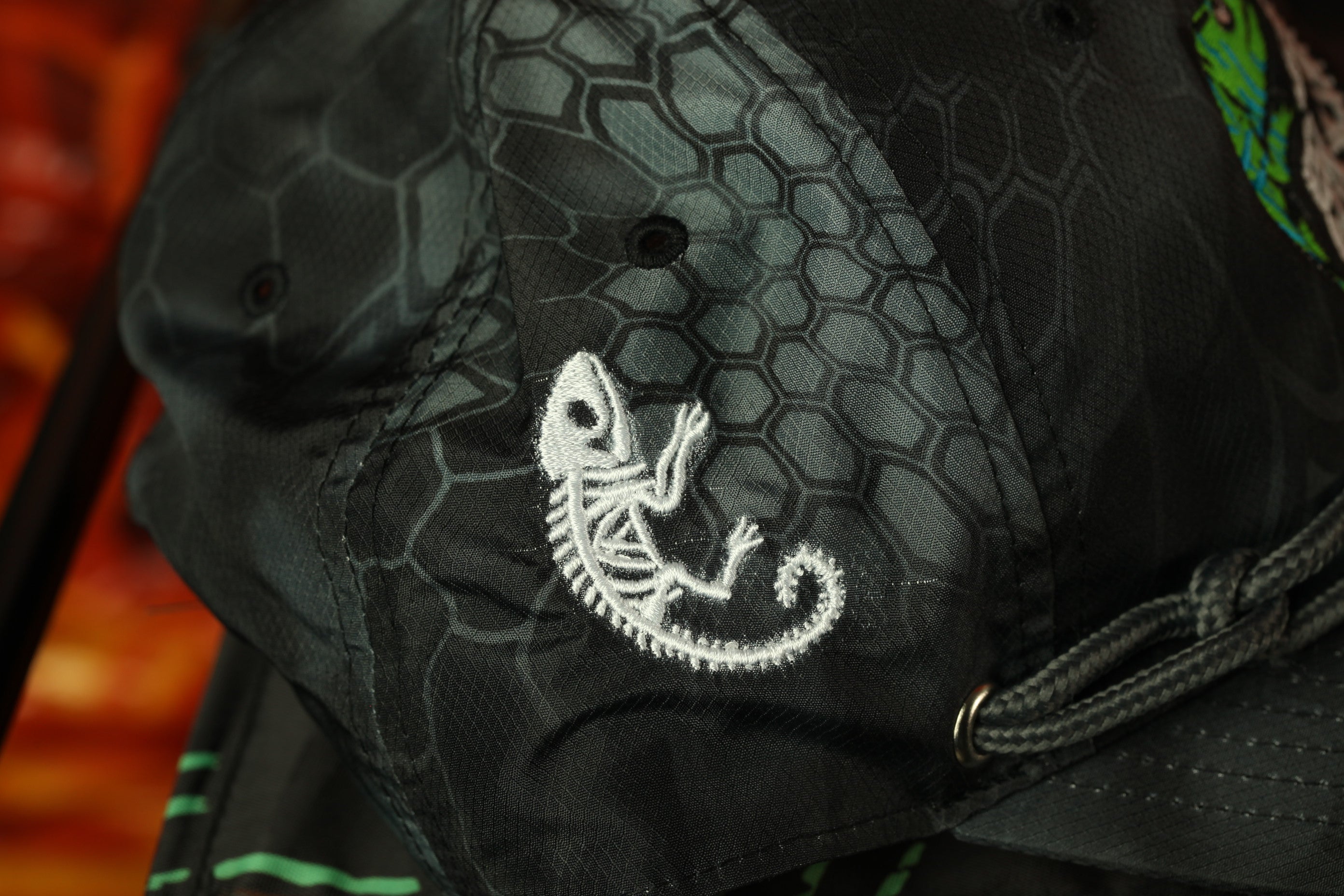 A close-up view of a black and gray patterned fabric, with a white embroidered design of a lizard or chameleon on the fabric.