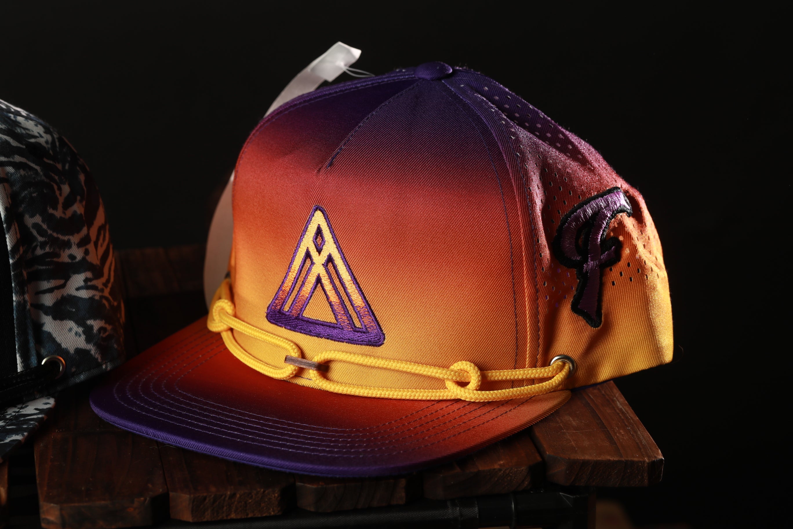 A colorful, gradient-colored baseball cap with a triangle logo on the front, resting on a wooden surface.