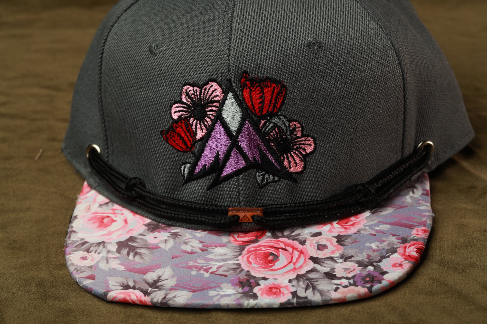 A gray baseball cap with a floral pattern on the brim and a black strap.