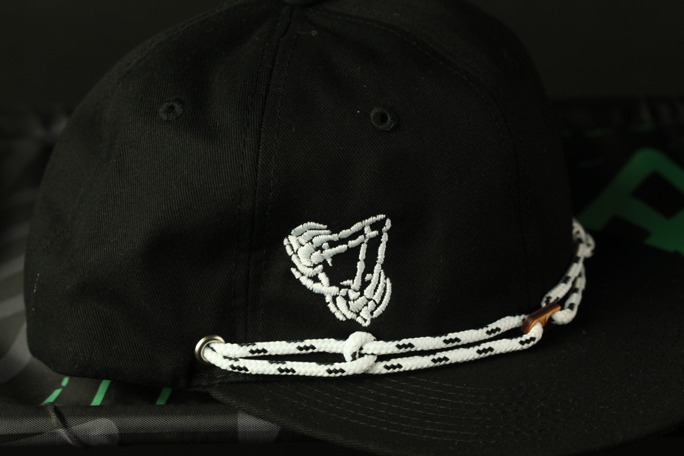 A black baseball cap with a white rope or chain strap and a white skull or skeleton design on the front.