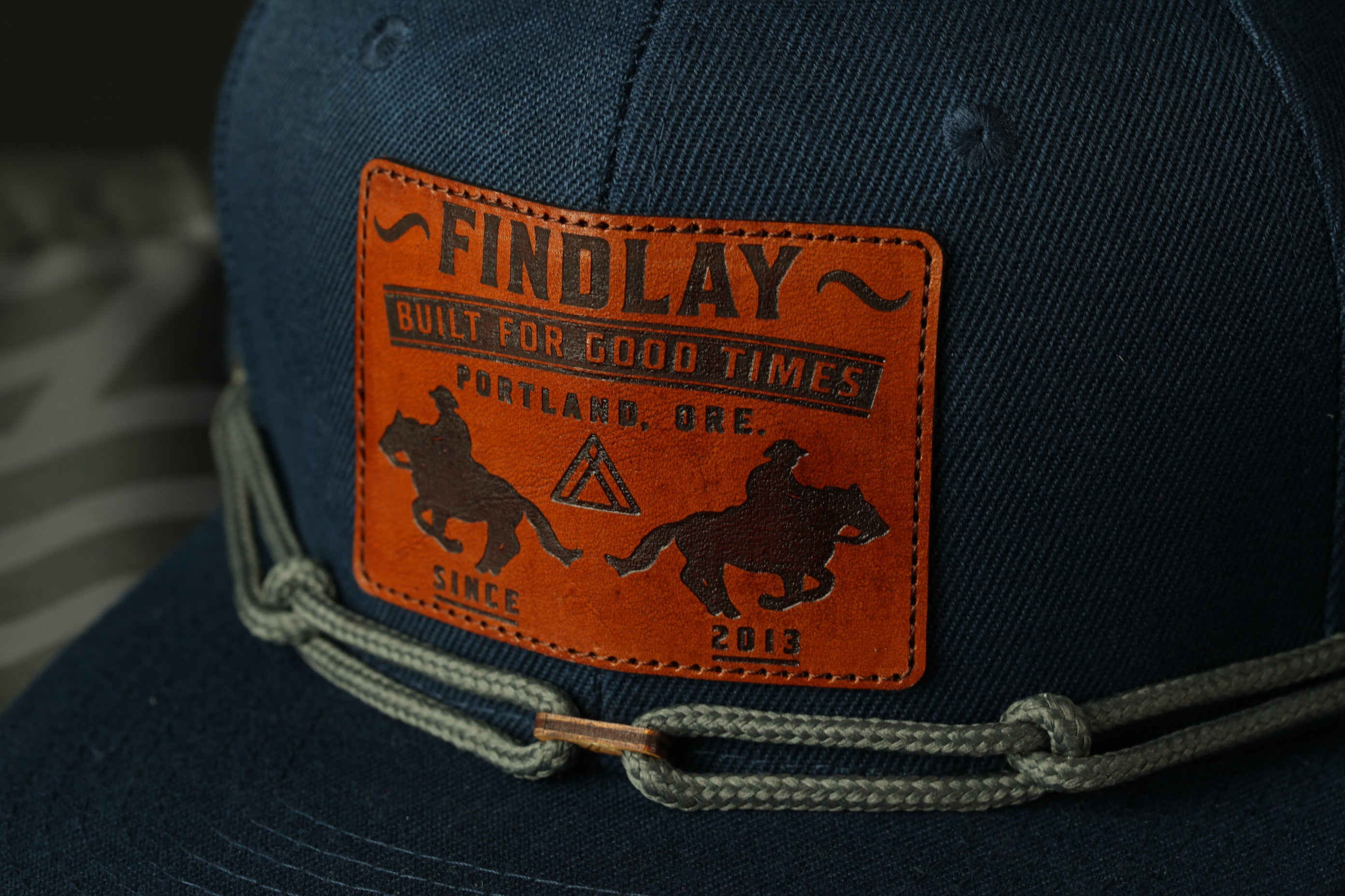A close-up of a dark blue baseball cap with a patch featuring text and an image of a person riding a horse.