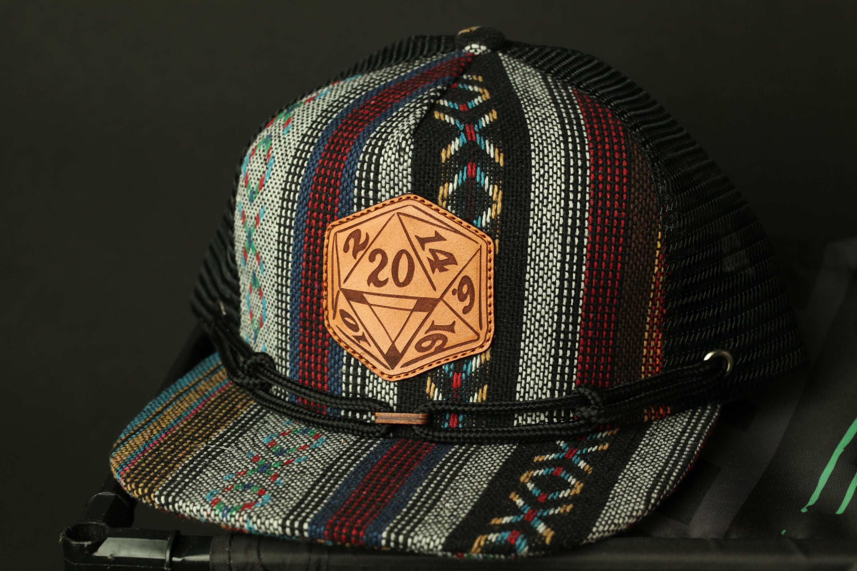 A colorful, patterned baseball cap with a leather patch on the front displaying a dice design.