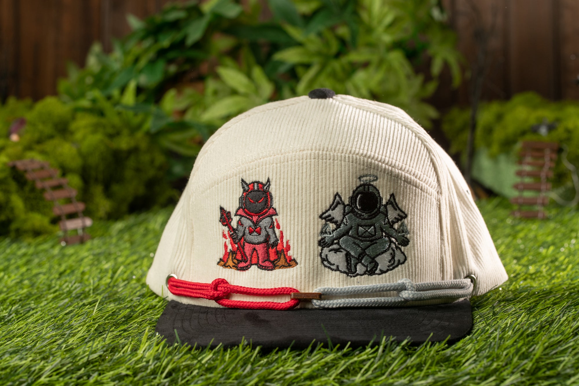 A white baseball cap with two cartoon characters on the front, one in red and one in black, sitting on a grassy surface.