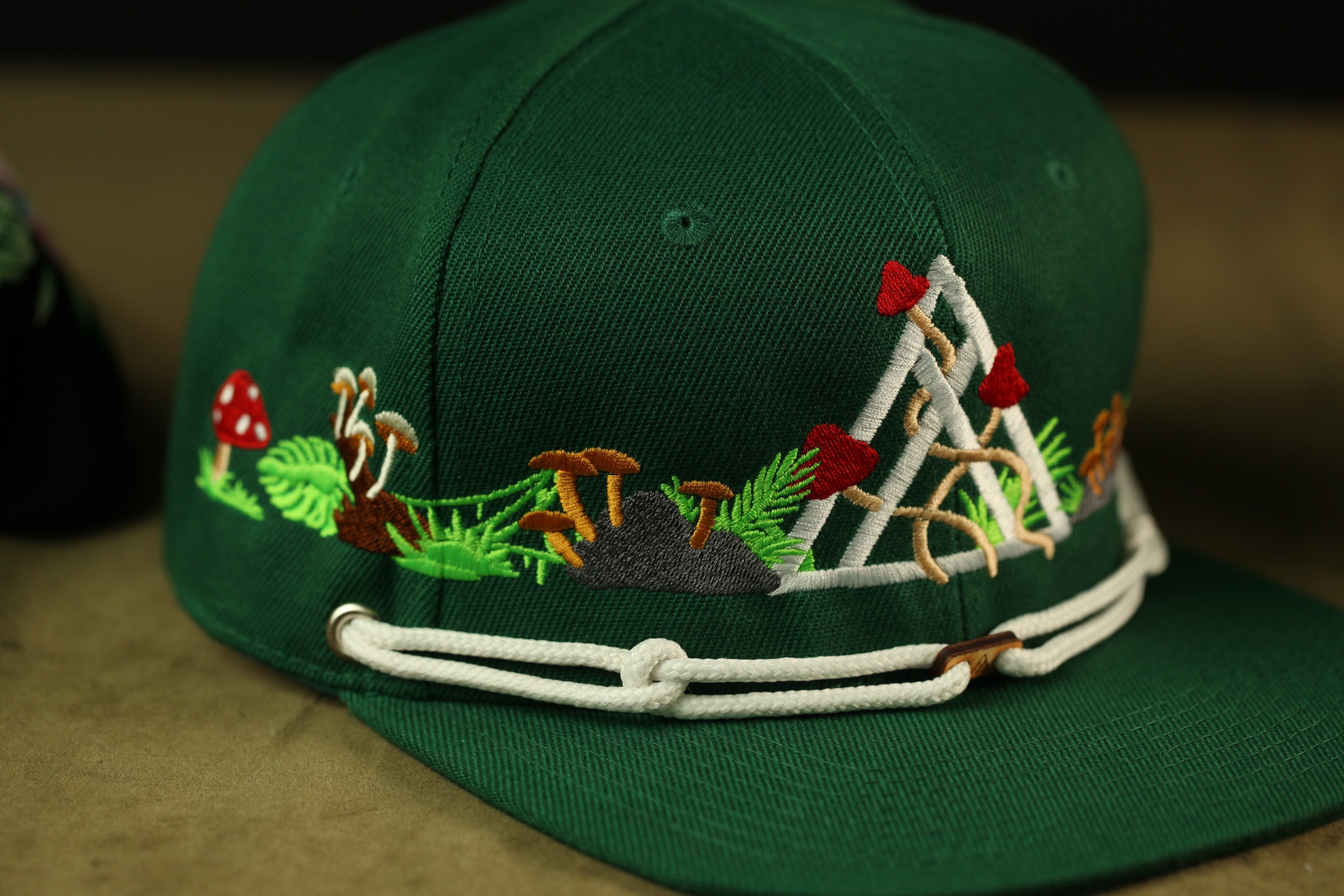 A close-up view of a green baseball cap with a floral pattern and mushrooms on the brim.