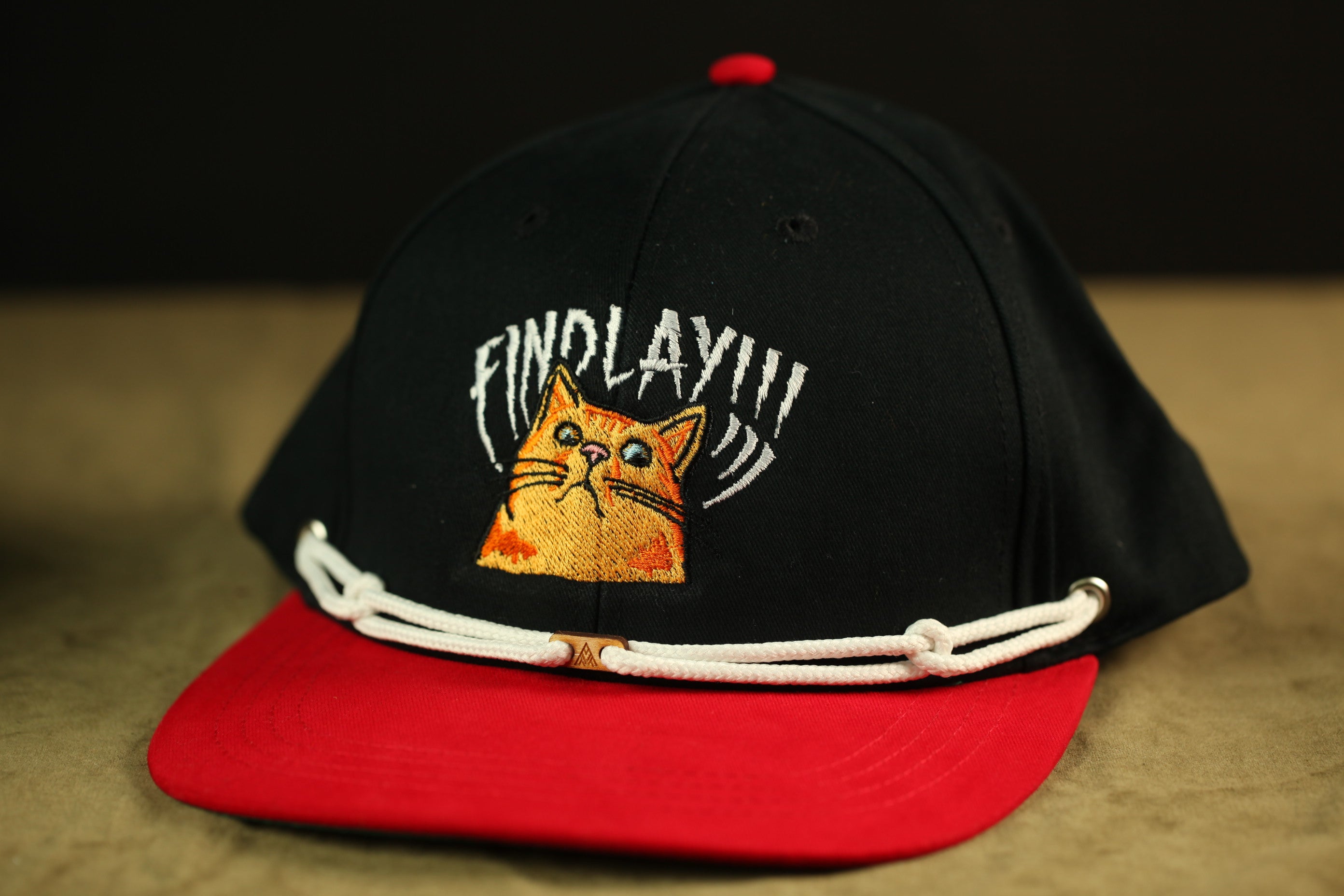 A black baseball cap with a red brim and a cat embroidered on the front.