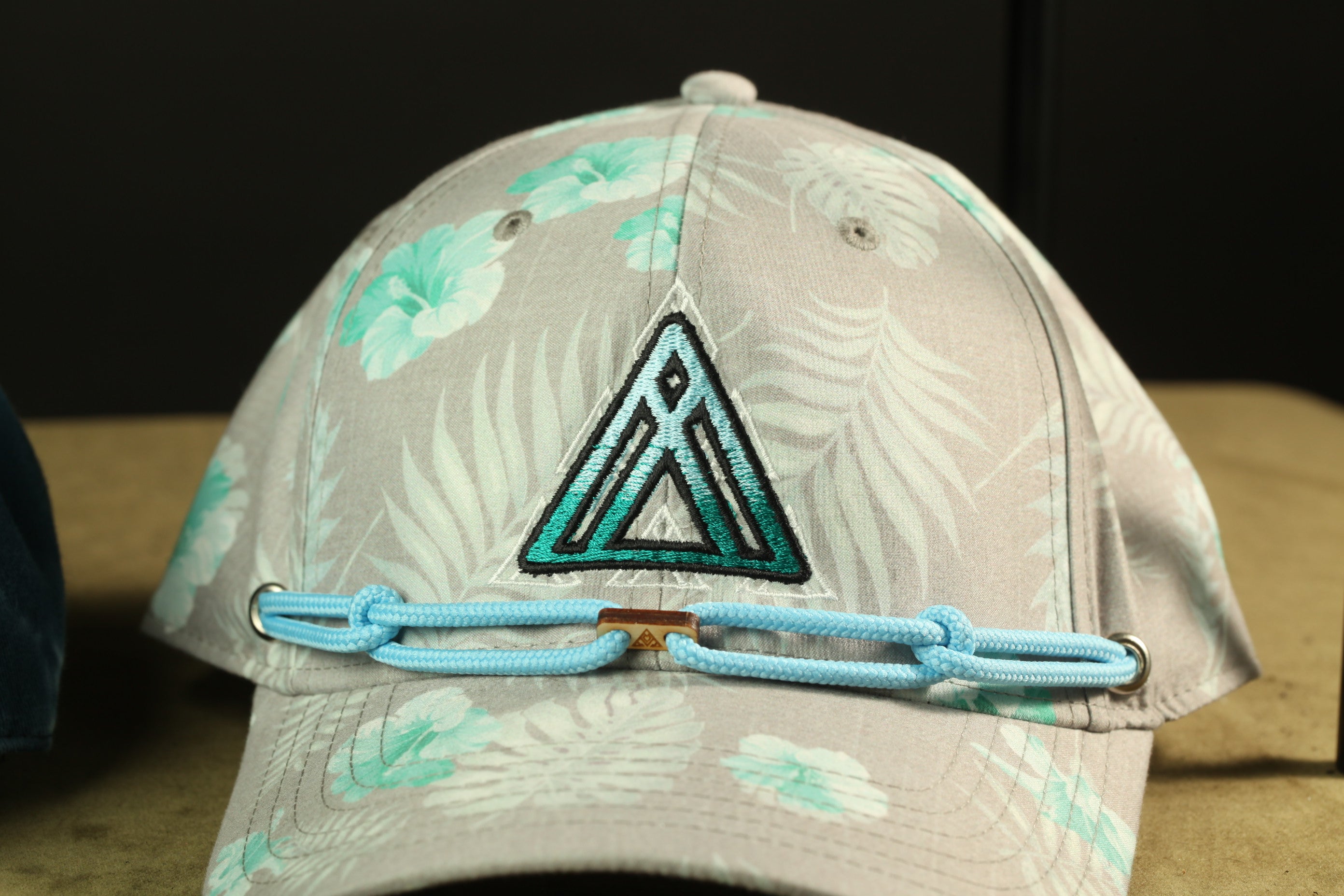 A gray baseball cap with a floral pattern and a triangular logo on the front.