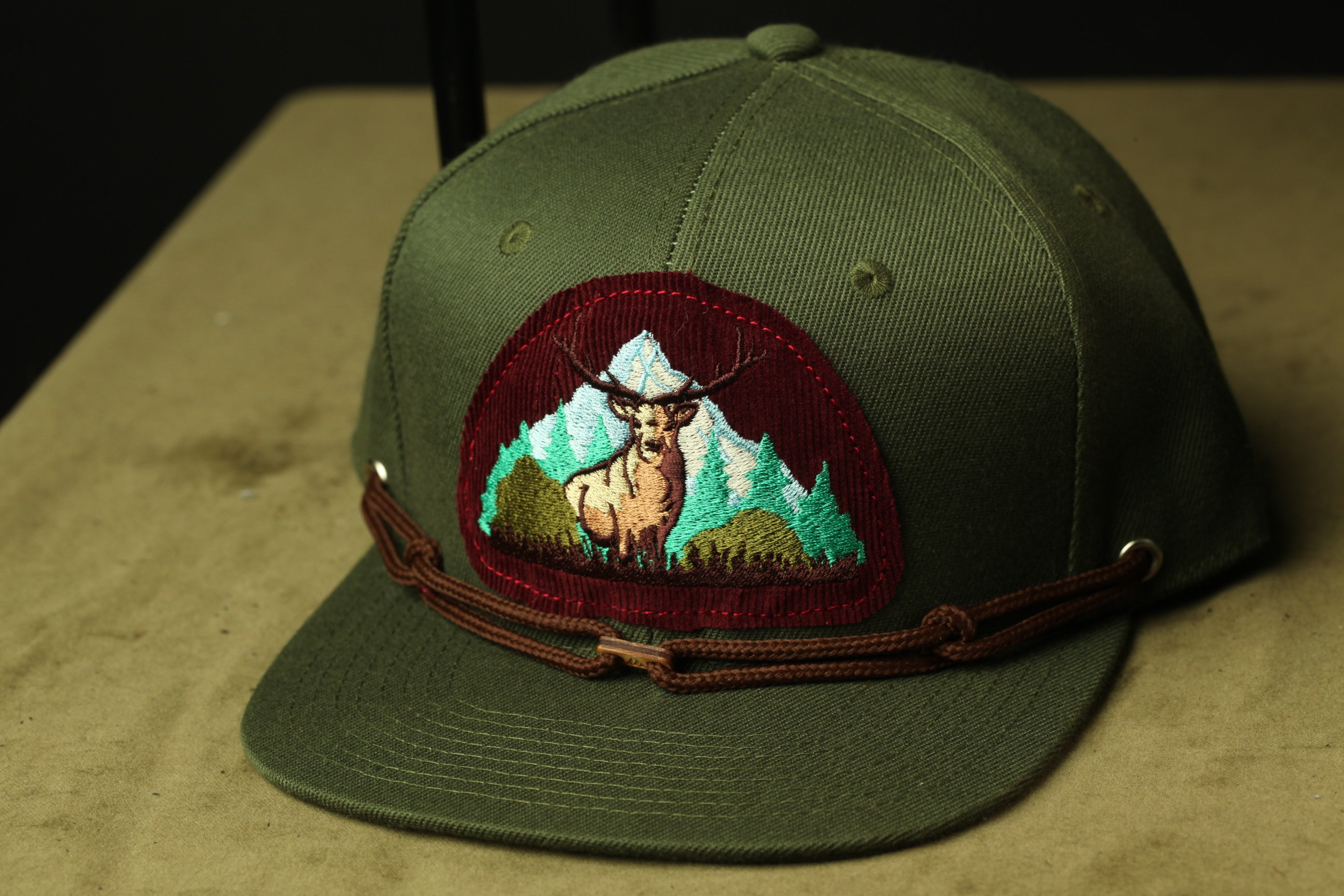 A green baseball cap with a red patch featuring a deer and mountains on it.