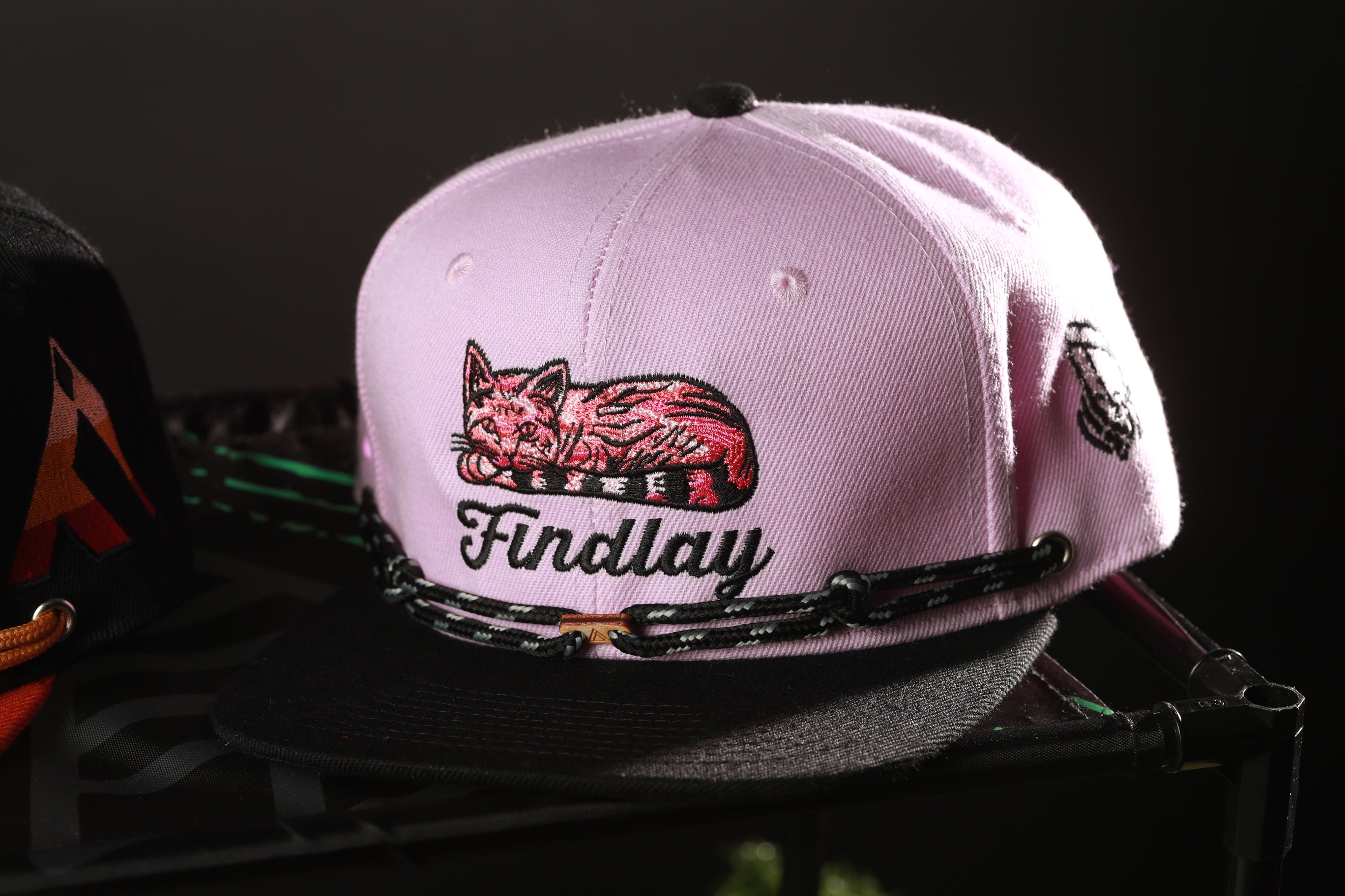 A pink baseball cap with a cat design and the word "Findlay" printed on it.
