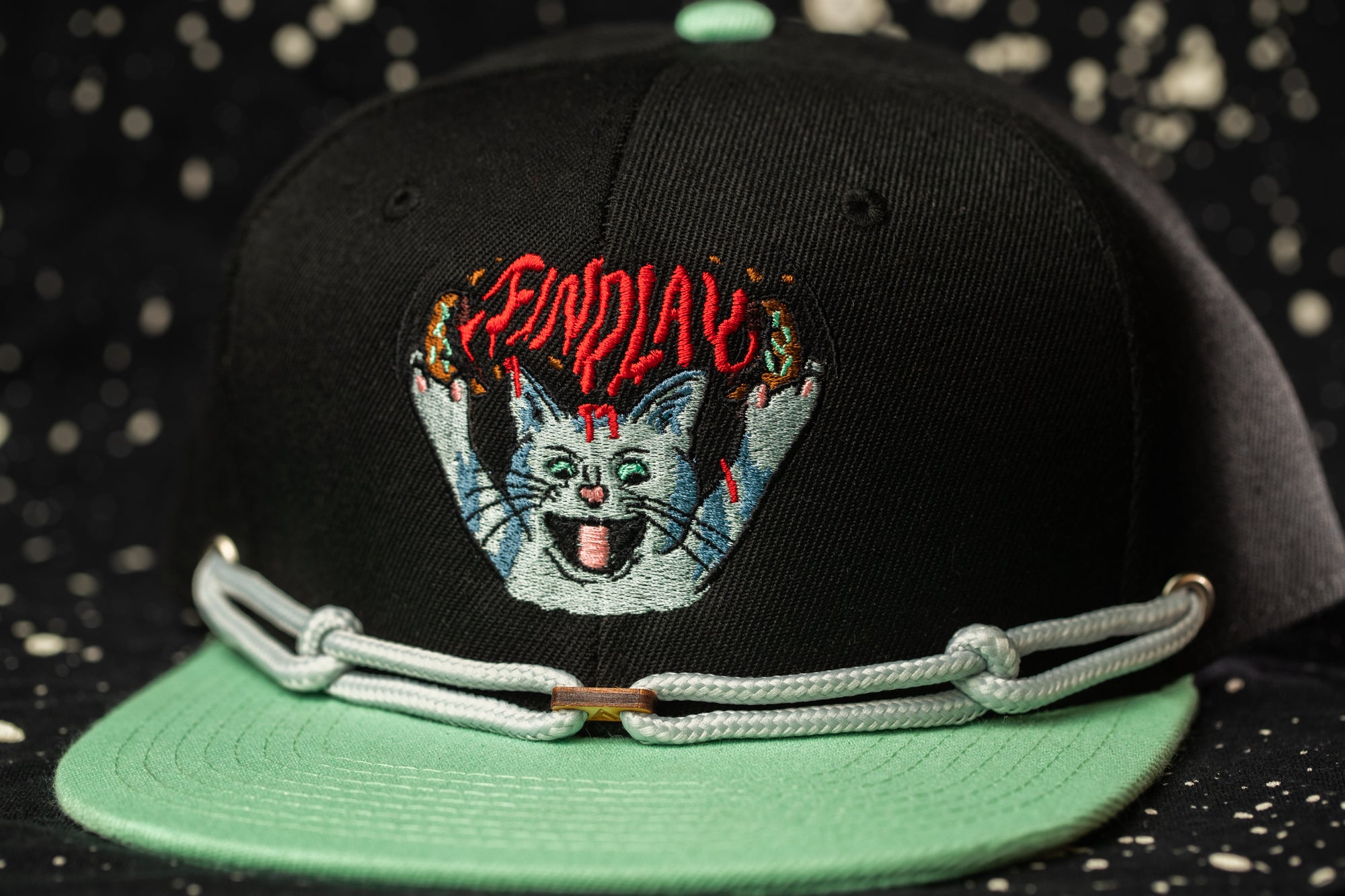 A black baseball cap with a green brim and a cat embroidered on the front.