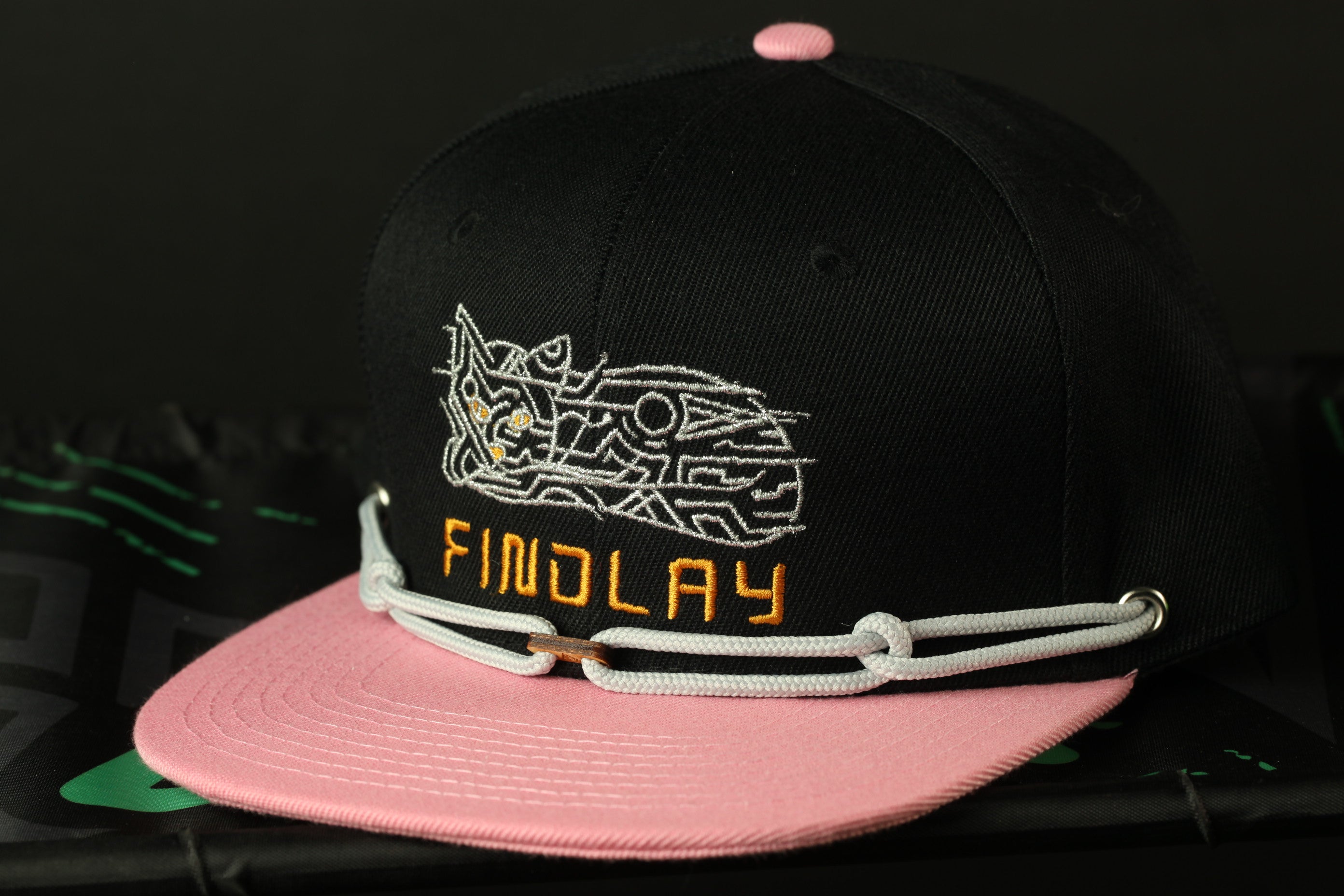 A black baseball cap with a pink brim and a white graphic design on the front.