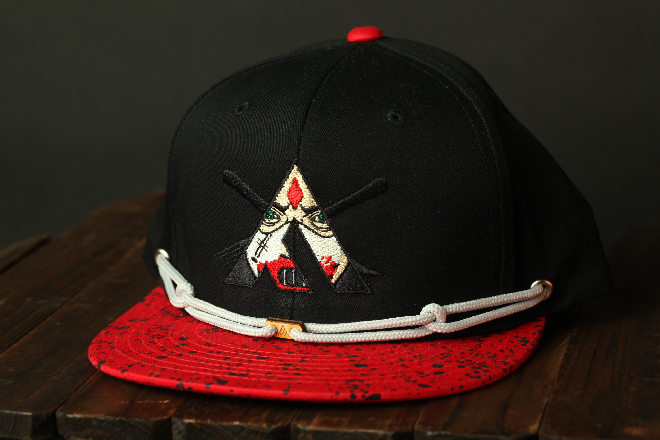 A black baseball cap with a red brim and a red and black patterned fabric, featuring a white logo with a red triangle and a red dot.