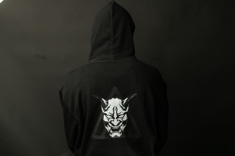 A person wearing a black hooded sweatshirt with a white graphic design on the back.