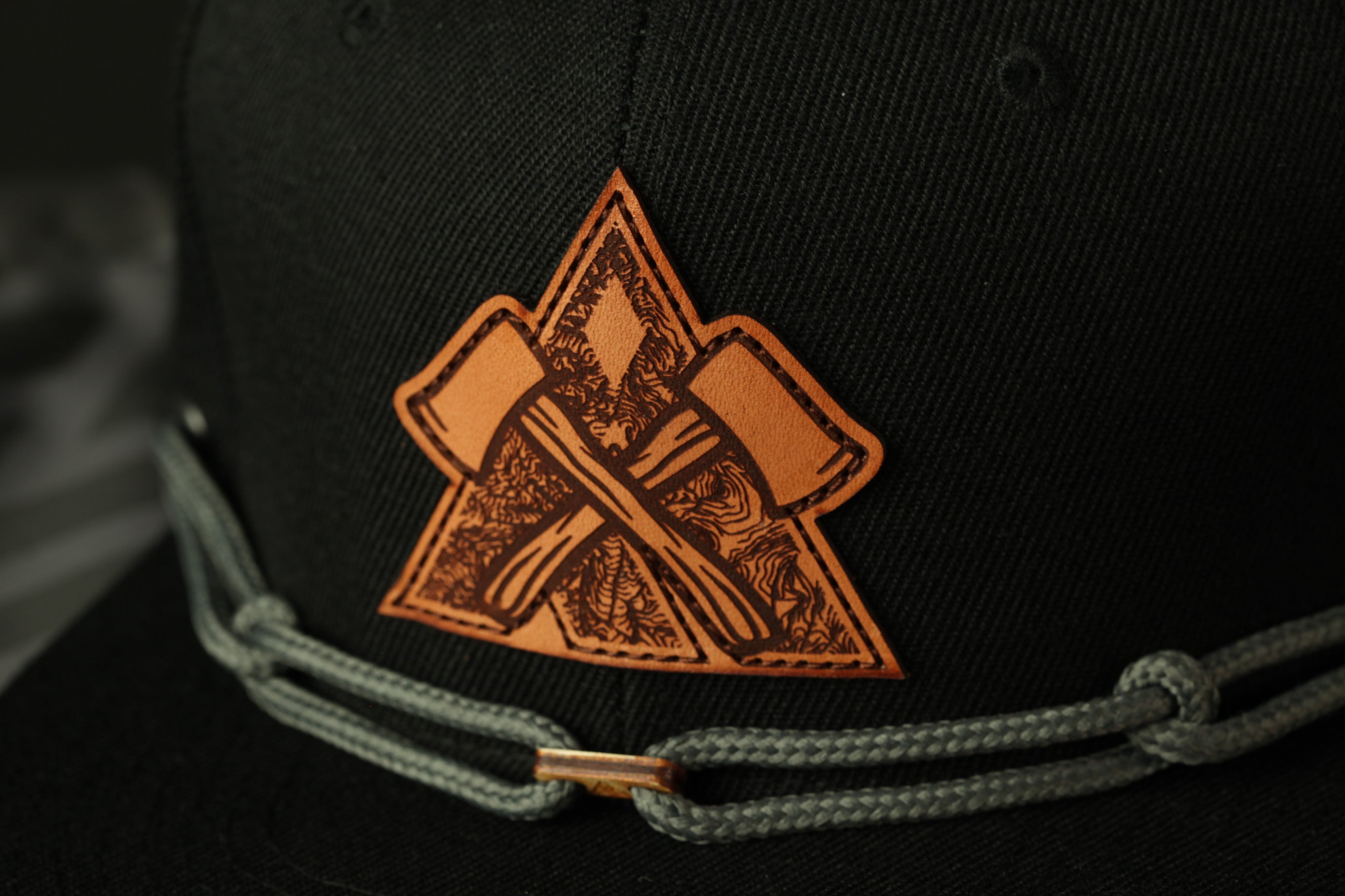 A close-up view of a black baseball cap with a leather patch featuring an intricate design.