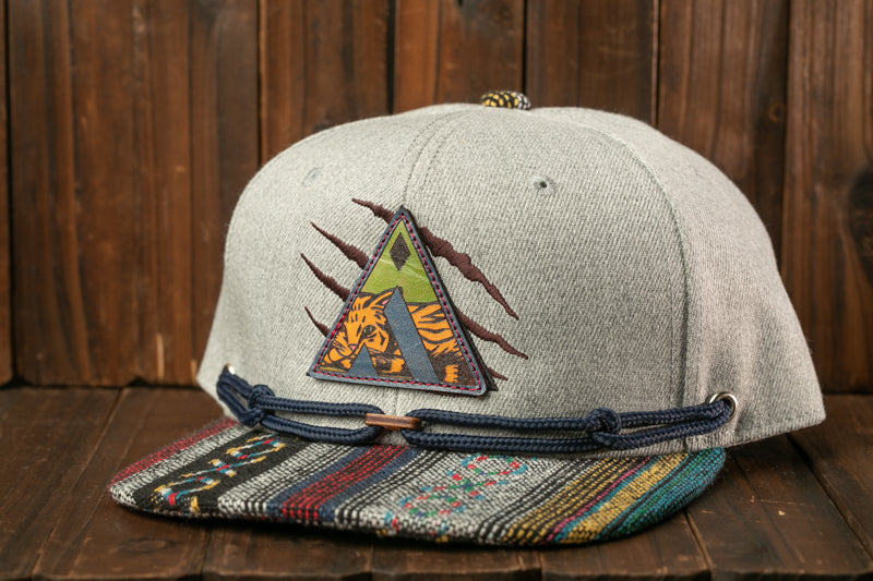 A gray baseball cap with a colorful, patterned brim and a patch featuring a tiger design, placed on a wooden surface.