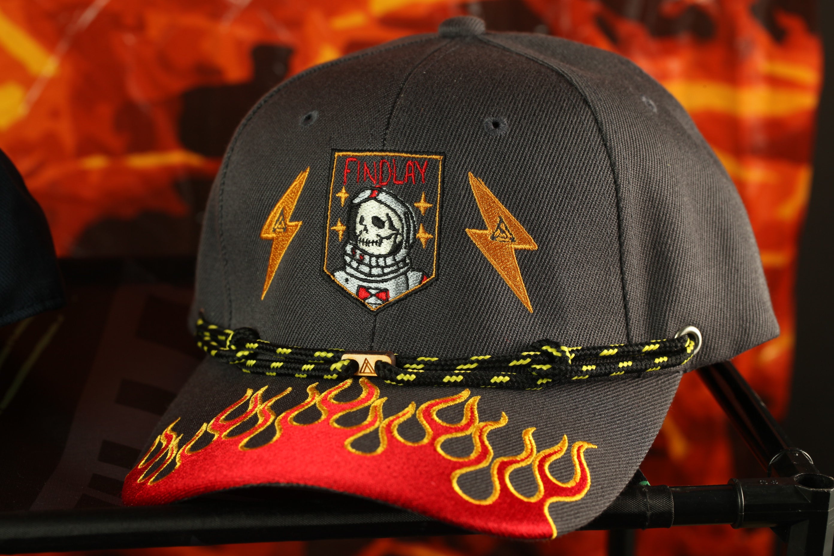 A black baseball cap with a flame-designed brim and a skull and lightning bolt patch on the front.