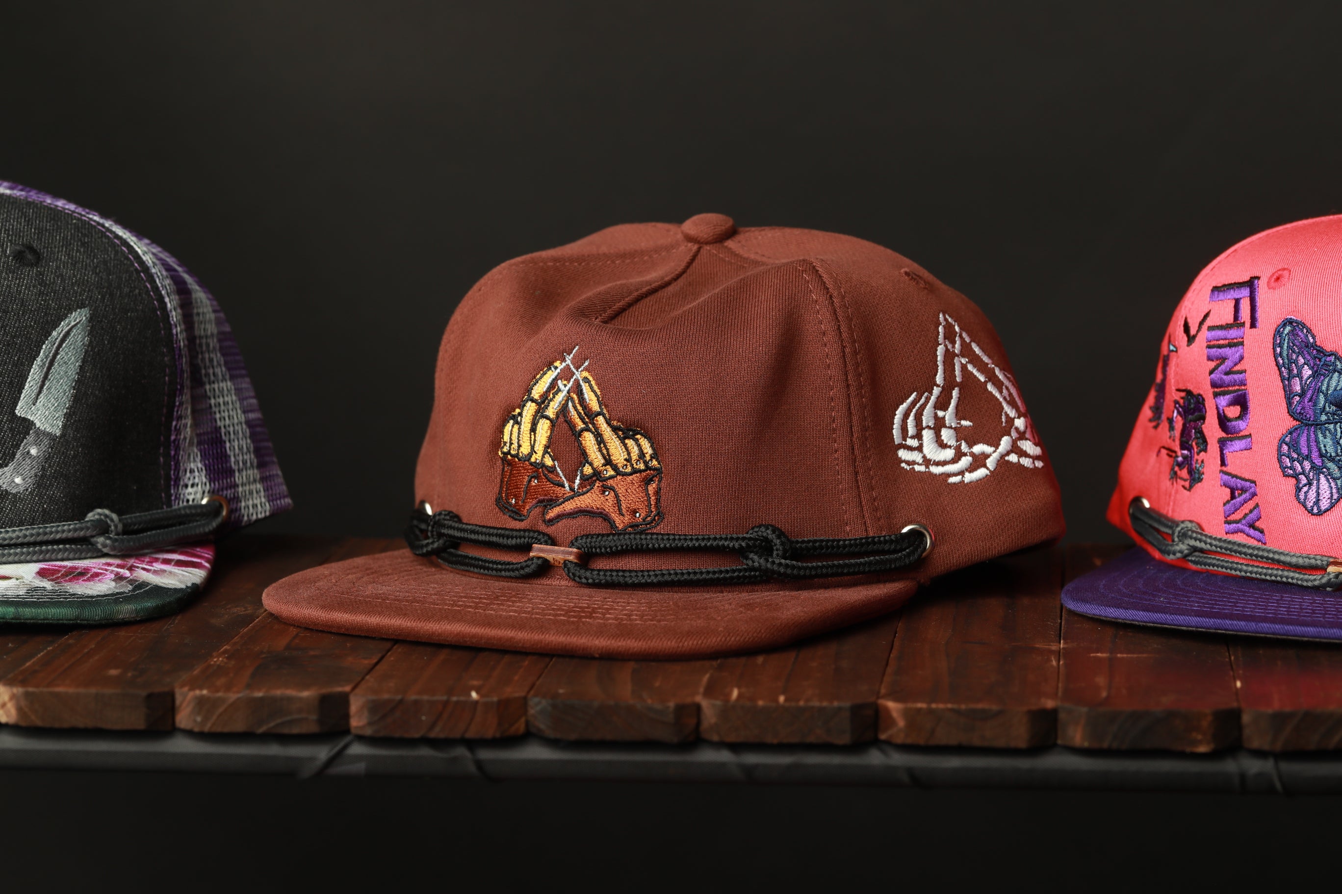 Three baseball caps are displayed on a wooden surface, each with unique designs and colors.