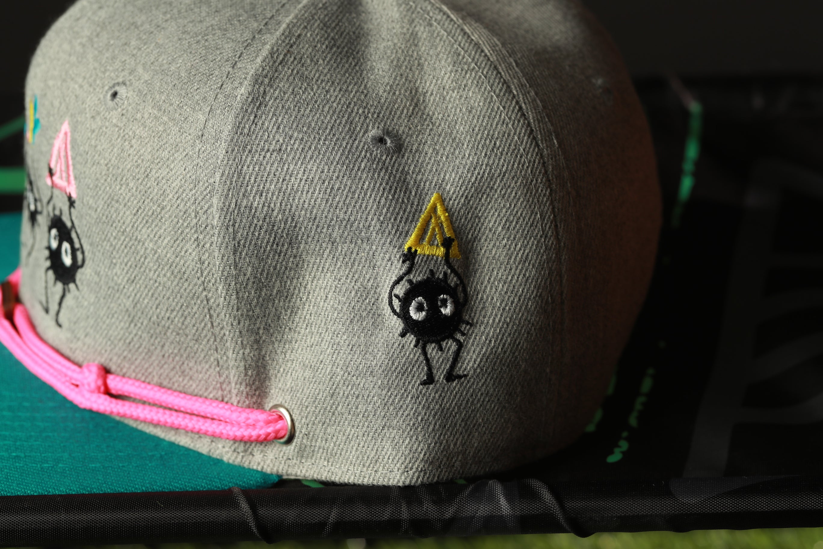 A gray baseball cap with a yellow triangle and a black spider-like character on it, sitting on a green surface.