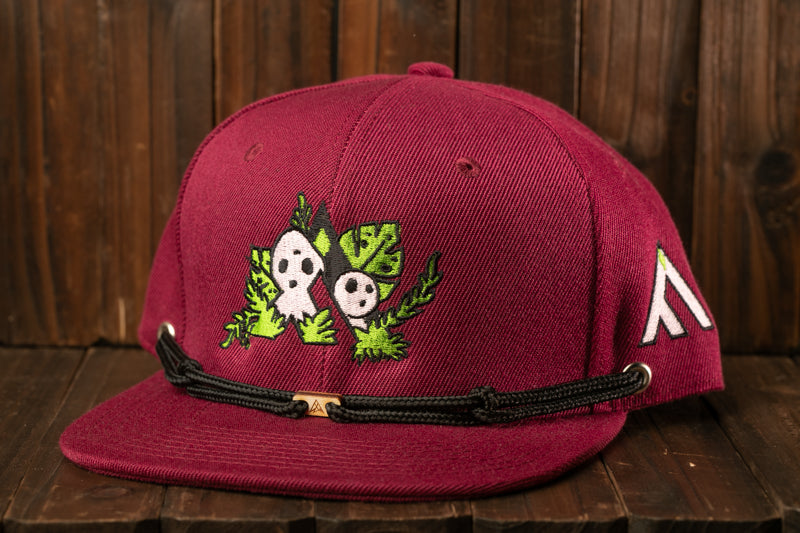 A maroon baseball cap with a graphic design featuring two cartoon-like faces and green leaves.